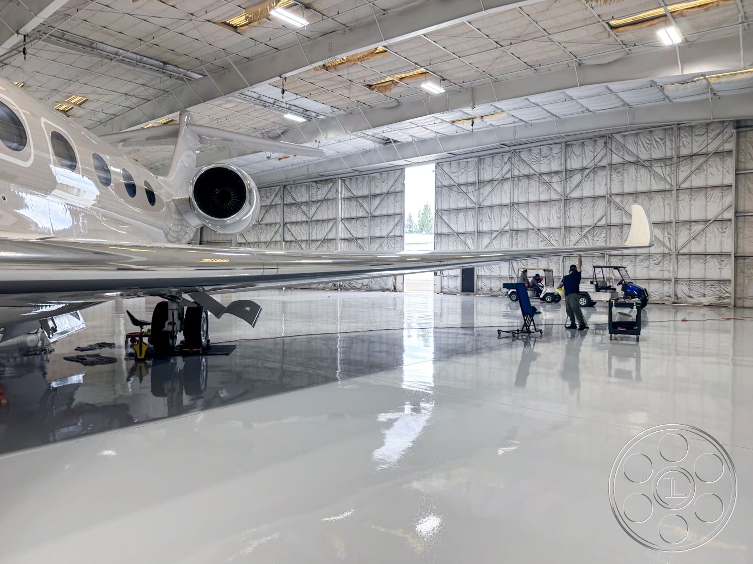 VN Hangar - open floor plan, mechanical equipment area, insulated wall panels, aircraft maintenance area, high ceiling with exposed trusses, interior hangar space, reflective epoxy floor coating, metal aircraft hangar structure, large glass hangar doors, strategically placed LED lighting fixtures, hangar with natural light, engineering workspace, safety signage on walls, tool storage areas, professional aviation environment