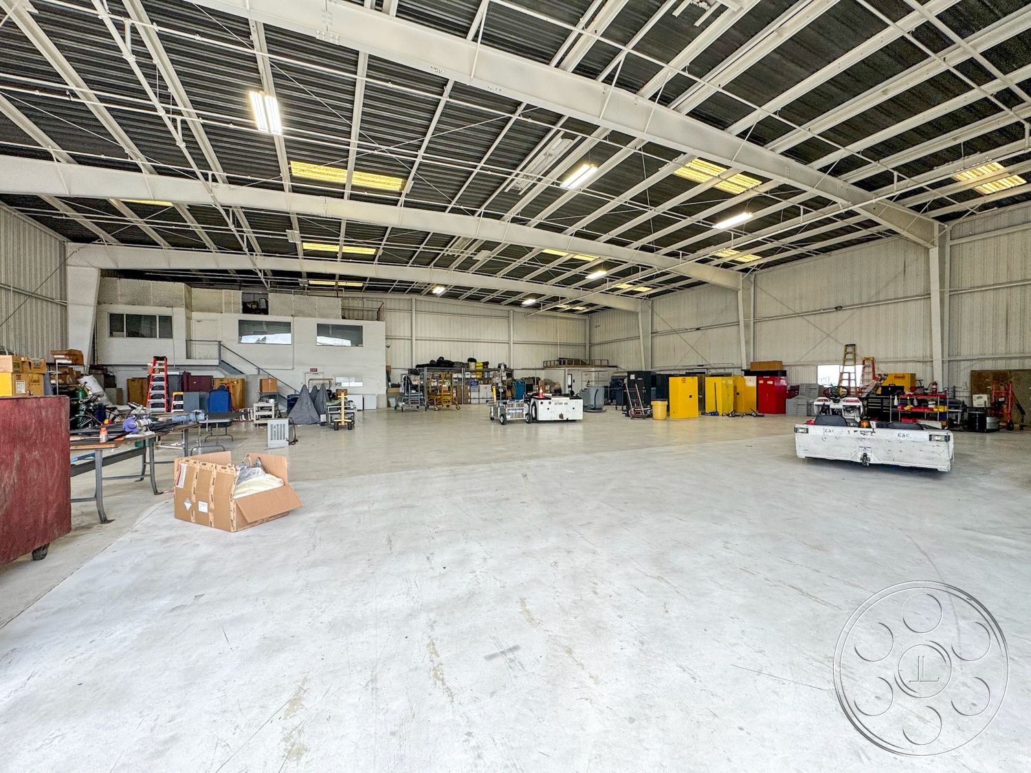 VN Hangar - open floor plan, concrete floor, utility area, large sliding doors, flat roof structure, functional work environment, metal storage cabinets, high ceiling interior, exposed metal beam ceiling, industrial warehouse space, administrative office area, painted drywall interior walls, glass block window inserts, stainless steel workshop tables, workshop lighting fixtures, unfinished industrial design, heavy-duty shelving units, commercial-grade flooring, spacious storage zone