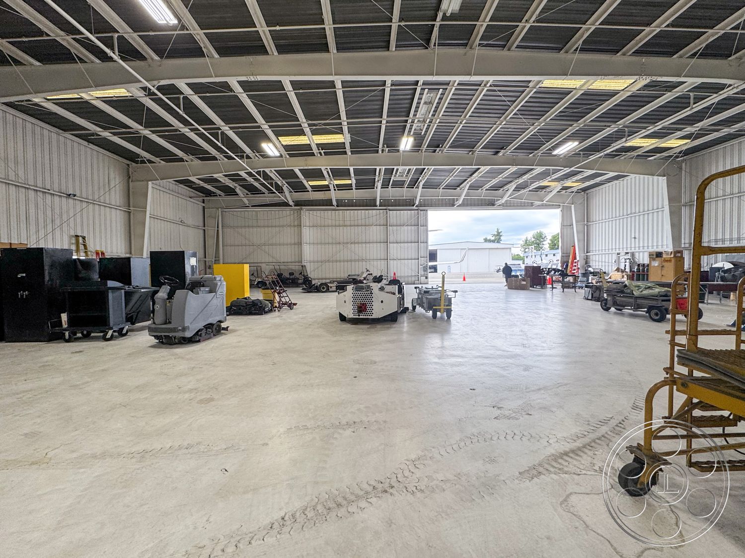 VN Hangar - open space layout, high vaulted ceiling, concrete floor slab, industrial warehouse interior, minimalist industrial design, metal roof panels, commercial storage area, roller door access, exterior steel frame construction, exposed steel trusses, proper lighting fixtures, large overhead garage door, concrete walls with insulation, functional layout for equipment storage, ventilation system detail