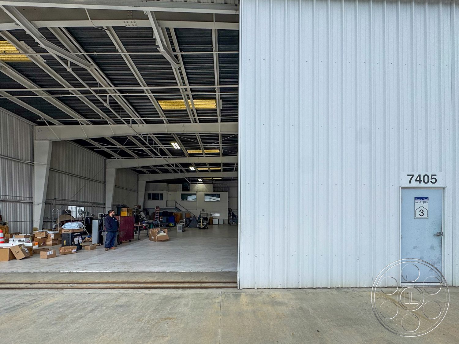 VN Hangar - industrial lighting fixtures, commercial building, open layout design, steel frame construction, concrete slab flooring, interior workspace, urban industrial setting, exposed structural beams, high ceiling warehouse space, metal panel exterior, large roll-up door entrance, gleaming concrete floors, partitioned office area, warehouse storage shelving, utility space function, exterior loading dock, dimensional steel siding, multilevel storage area, oversized windows for natural light