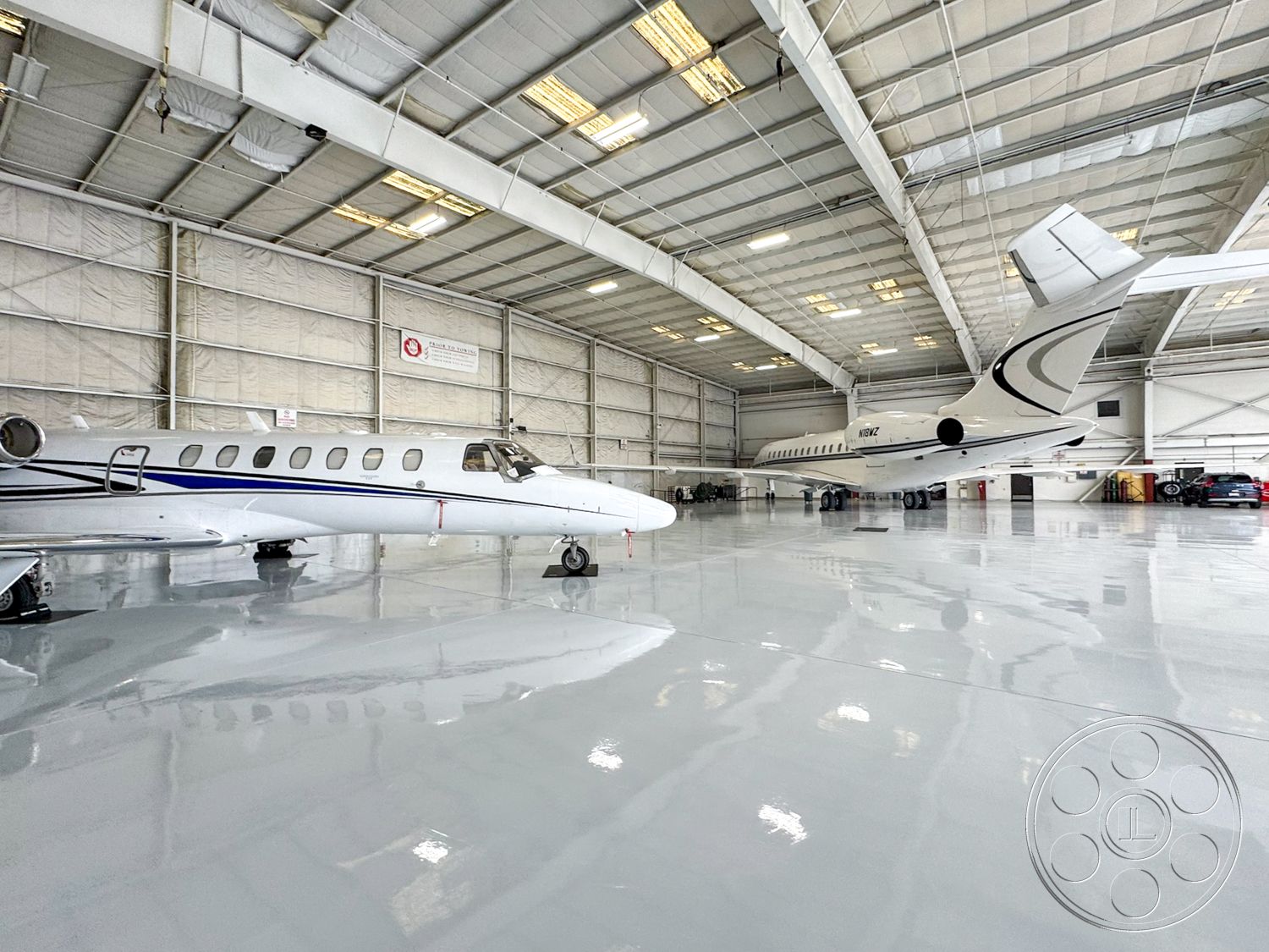 VN Hangar - glass doors, contemporary design elements, minimalist interior design, white painted walls, fluorescent lighting fixtures, vehicle parking area, concrete polished flooring, aircraft maintenance zone, exterior airplane hangar, metal structure with high ceilings, industrial steel support beams, aluminum frame windows, tall sliding hangar doors, insulated fabric wall panels, open space for aircraft storage, hangar with easy access to runways, well-lit hangar area