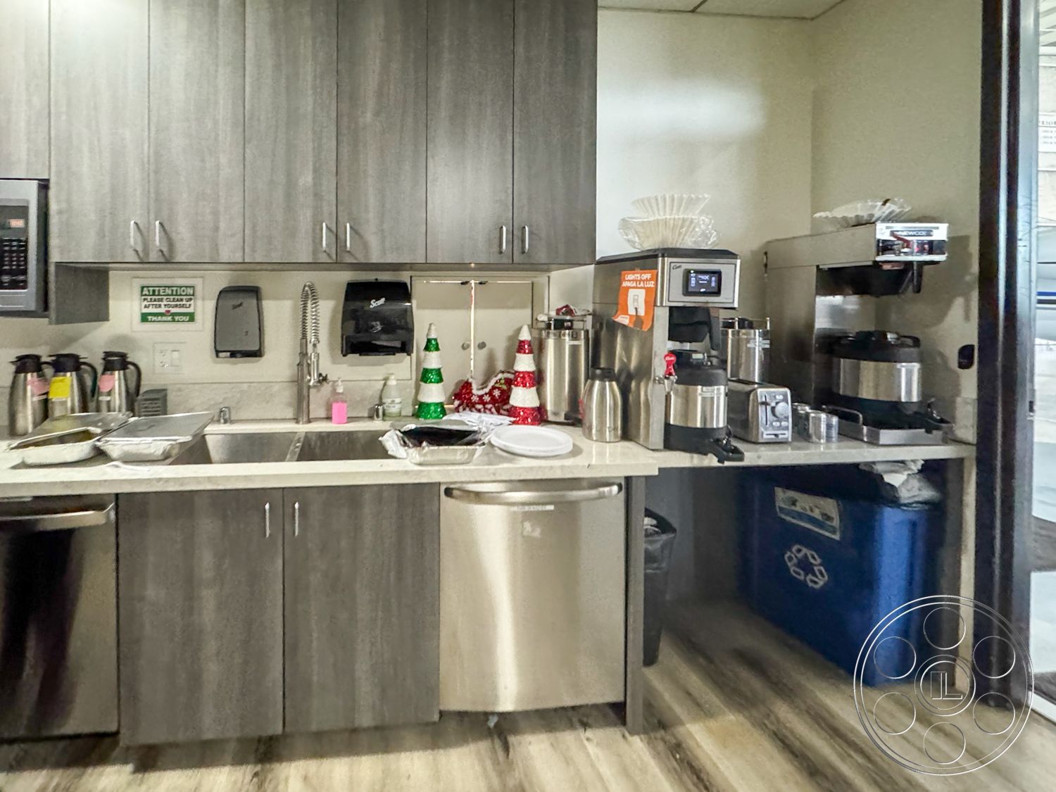 VN Hangar - textured flooring, granite countertop, safety signage, stainless steel refrigerator, overhead fluorescent lighting, interior kitchen, stainless steel dishwasher, wall-mounted soap dispenser, gray laminate cabinetry, double sink workstation, commercial coffee maker, plastic serving trays, metal beverage dispensers, white dishware, decorative holiday decor