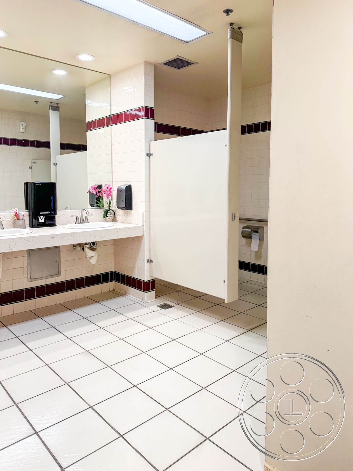 VN Hangar - framed mirror, chrome faucet, white solid surface countertop, minimalist bathroom design, tile bathroom flooring, fluorescent ceiling lights, white ceramic wall tiles, red accent tile border, stall partition walls, modern restroom interior, sink area with soap dispenser, commercial restroom setting