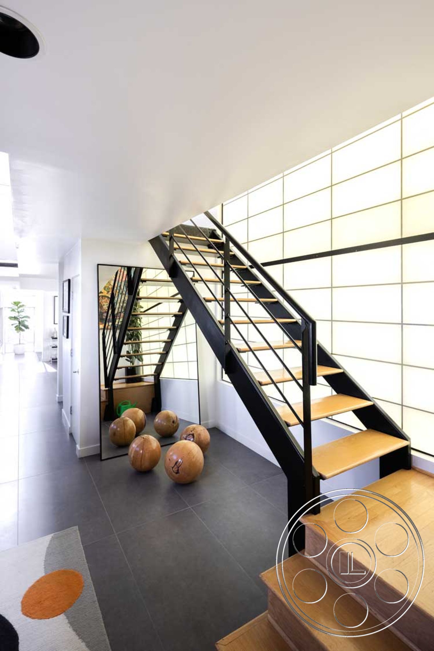 Modern 56 - open concept living space, white painted walls, smooth ceiling with recessed lighting, contemporary architectural details, glass wall panels, natural light filled corridor, minimalist entryway design, interior staircase with black steel railings, oak wood stair treads, matte gray tile flooring, decorative wood bowl decor, modern minimalism style, floor-to-ceiling window feature