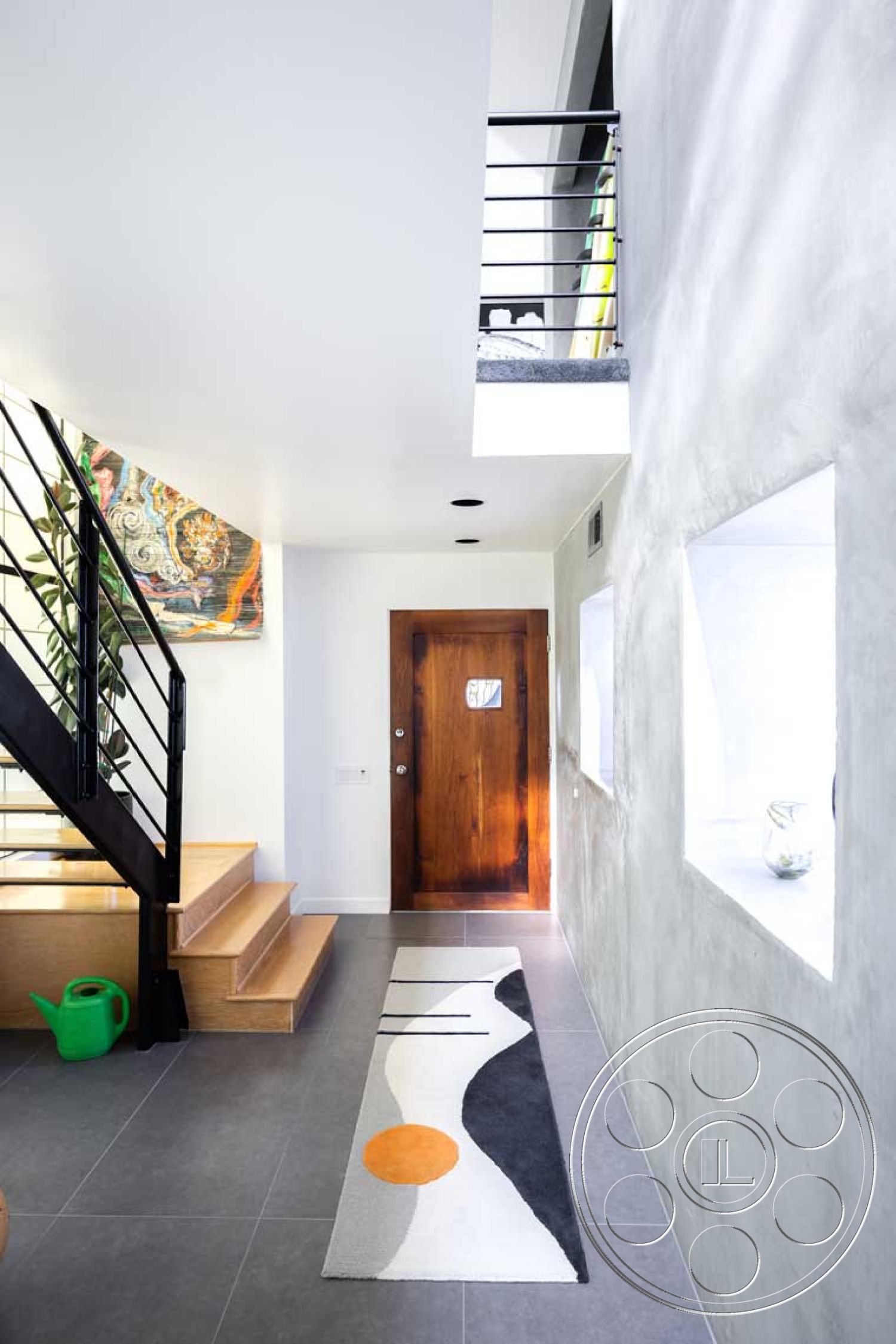 Modern 56 - artistic wall decor, minimalist design elements, exposed concrete wall, natural light from windows, slate tile flooring, wooden entry door, textured plaster wall treatment, contemporary staircase design, interior entrance hall, metal stair railings, modern area rug, natural wood stair treads, geometric rug pattern, bright foyer, open floor plan entryway, spaces defined by geometric shapes