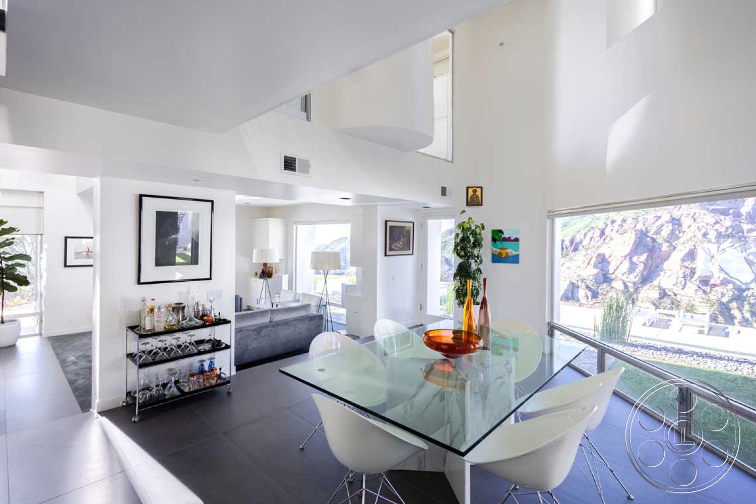 Modern 56 - high ceilings, minimalist decor, neutral color palette, minimalist design, stone accent wall, abstract wall art, modern light fixtures, open concept layout, floor-to-ceiling windows, textured wall panels, glass dining table, mountain view, modern kitchen island, natural light-filled space, white painted walls, stylish pendant lighting, potted indoor plants, dark ceramic tile flooring, white molded plastic chairs, contemporary bar cart