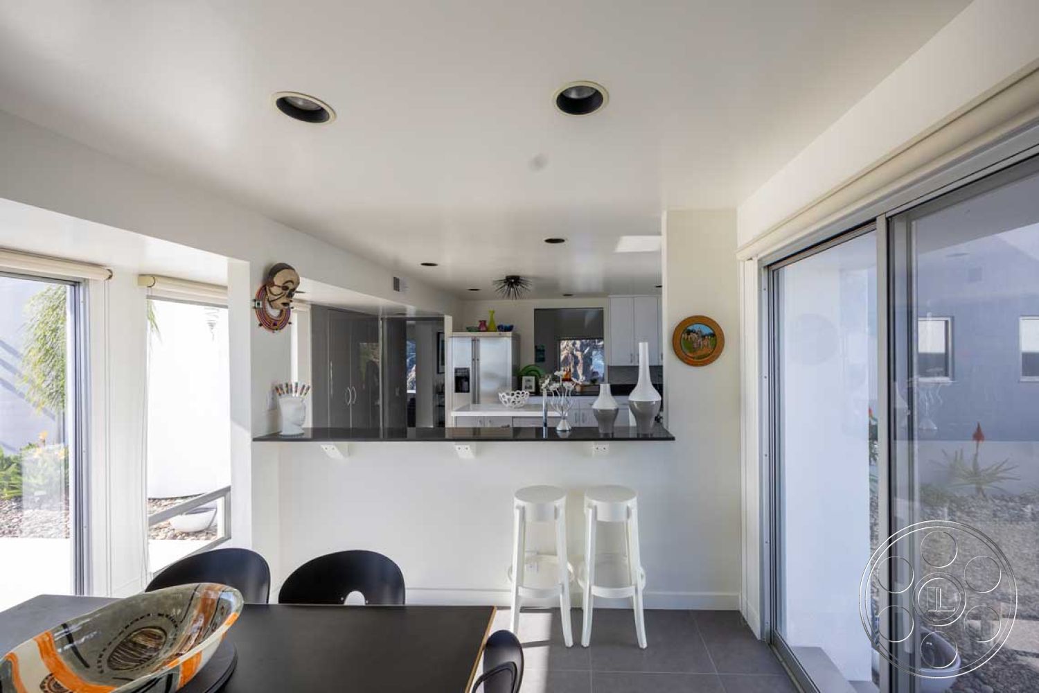 Modern 56 - stainless steel appliances, minimalist design elements, open concept layout, bar seating area, indoor-outdoor flow, floor-to-ceiling windows, rectangular dining table, bright color accents, concrete kitchen countertop, interior kitchen space, glass kitchen backsplash, natural light illumination, modern white cabinetry, tile kitchen floor, spotlight ceiling fixtures, geometric decor objects, potted plants decoration, wooden accent art pieces