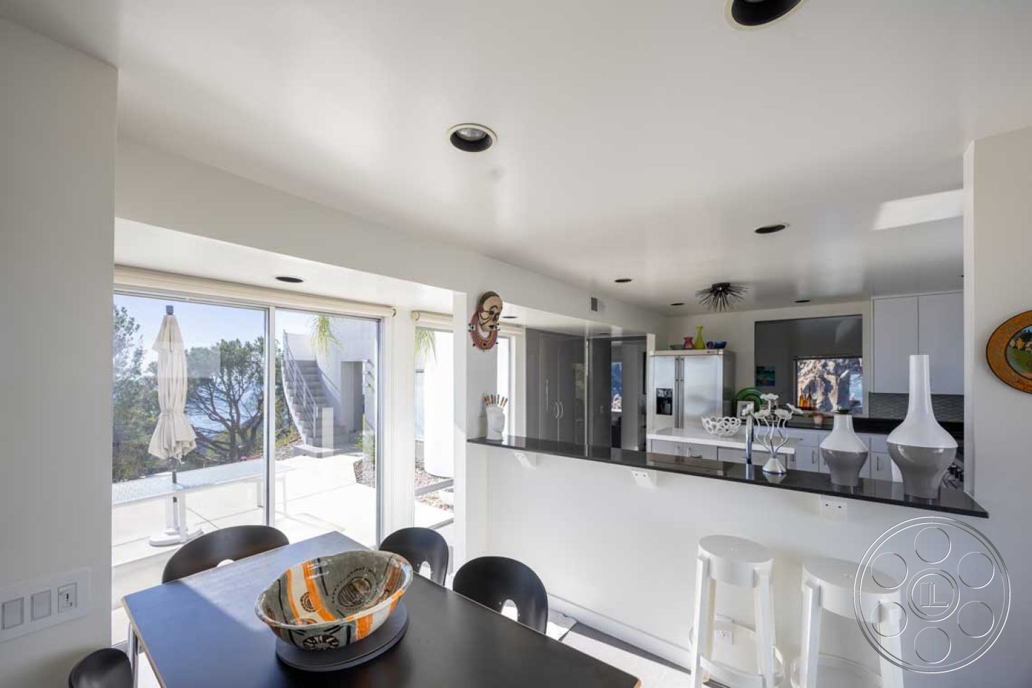 Modern 56 - minimalist decor, neutral color palette, light hardwood flooring, contemporary pendant lighting, decorative wall art, stainless steel refrigerator, modern dining table, open concept dining area, floor-to-ceiling glass sliding doors, view of landscaped garden, interior kitchen with white cabinetry, black granite countertop bar, ceramic vases on countertop, chrome kitchen appliances, seamless connection to outdoor patio, smooth painted ceiling, coastal setting with ocean view