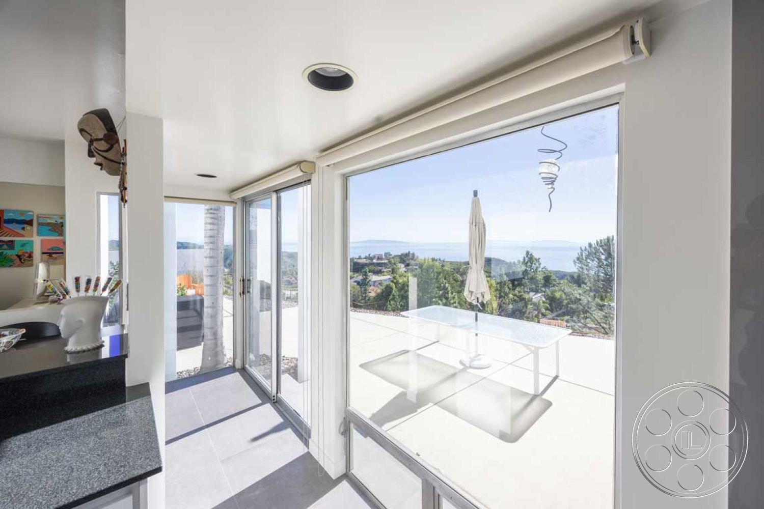 Modern 56 - interior floor-to-ceiling windows, interior white painted walls, interior minimalist design, interior open-concept living space, exterior landscaped surroundings, interior glass sliding doors, interior modern dining table, interior connection to outdoor space, exterior smooth stucco walls, exterior concrete patio, interior porcelain tile flooring, interior artistic wall decor, interior soft natural light, exterior panoramic ocean view, interior dark granite kitchen countertops, interior contemporary pendant lighting, exterior outdoor umbrella