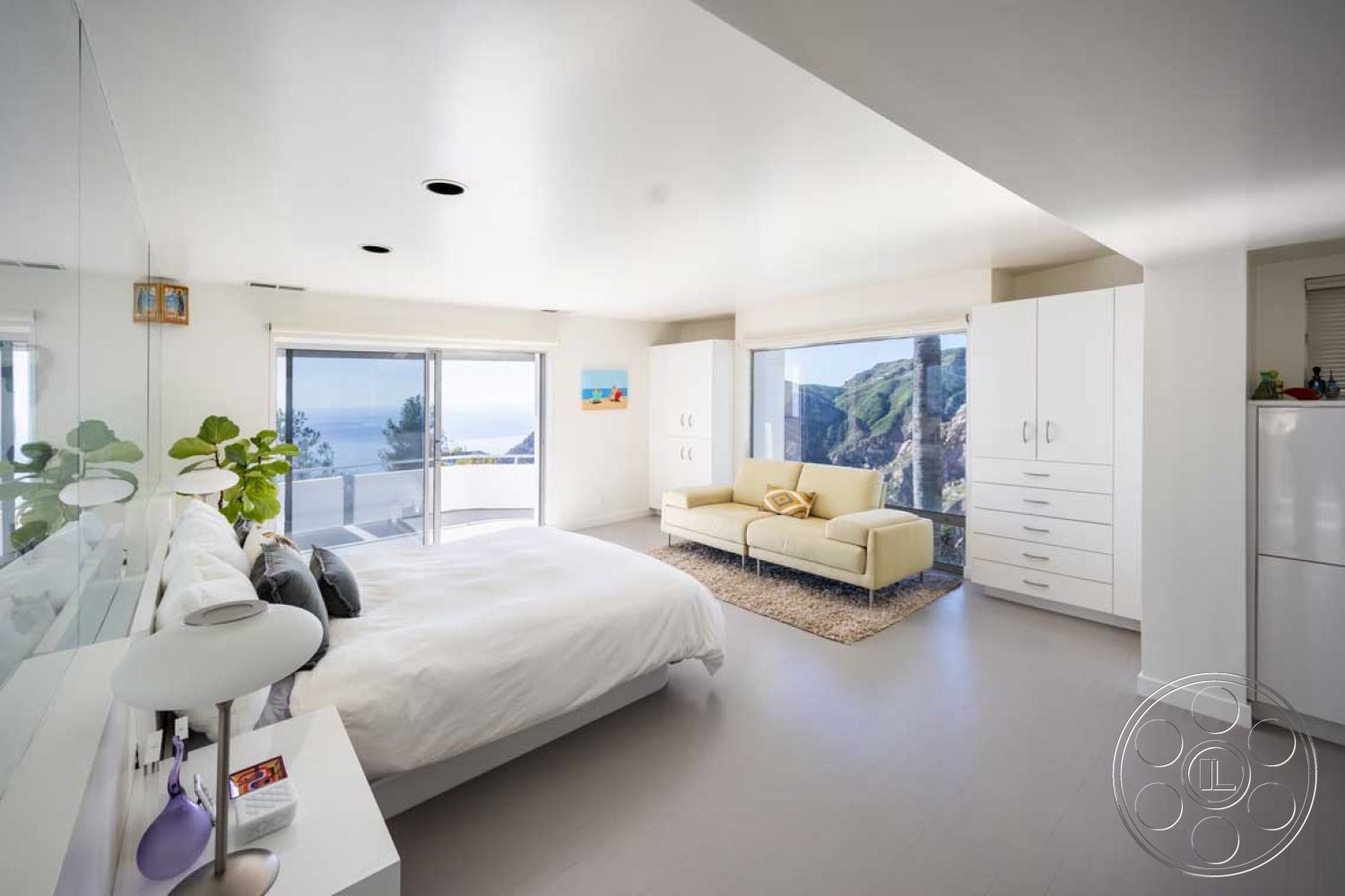 Modern 56 - natural light from floor-to-ceiling windows, interior bedroom with white painted walls, contemporary white cabinetry in bedroom, large glass sliding doors with ocean view, minimalist flooring with light-colored vinyl flooring, modern bed with white duvet and pillows, cozy sofa seating area in beige fabric, stylish area rug in neutral tones, contemporary indoor plant for décor, streamlined design with minimalist decor, cabinet storage with sleek handles, scenic mountain landscape view, open space design for airy feel