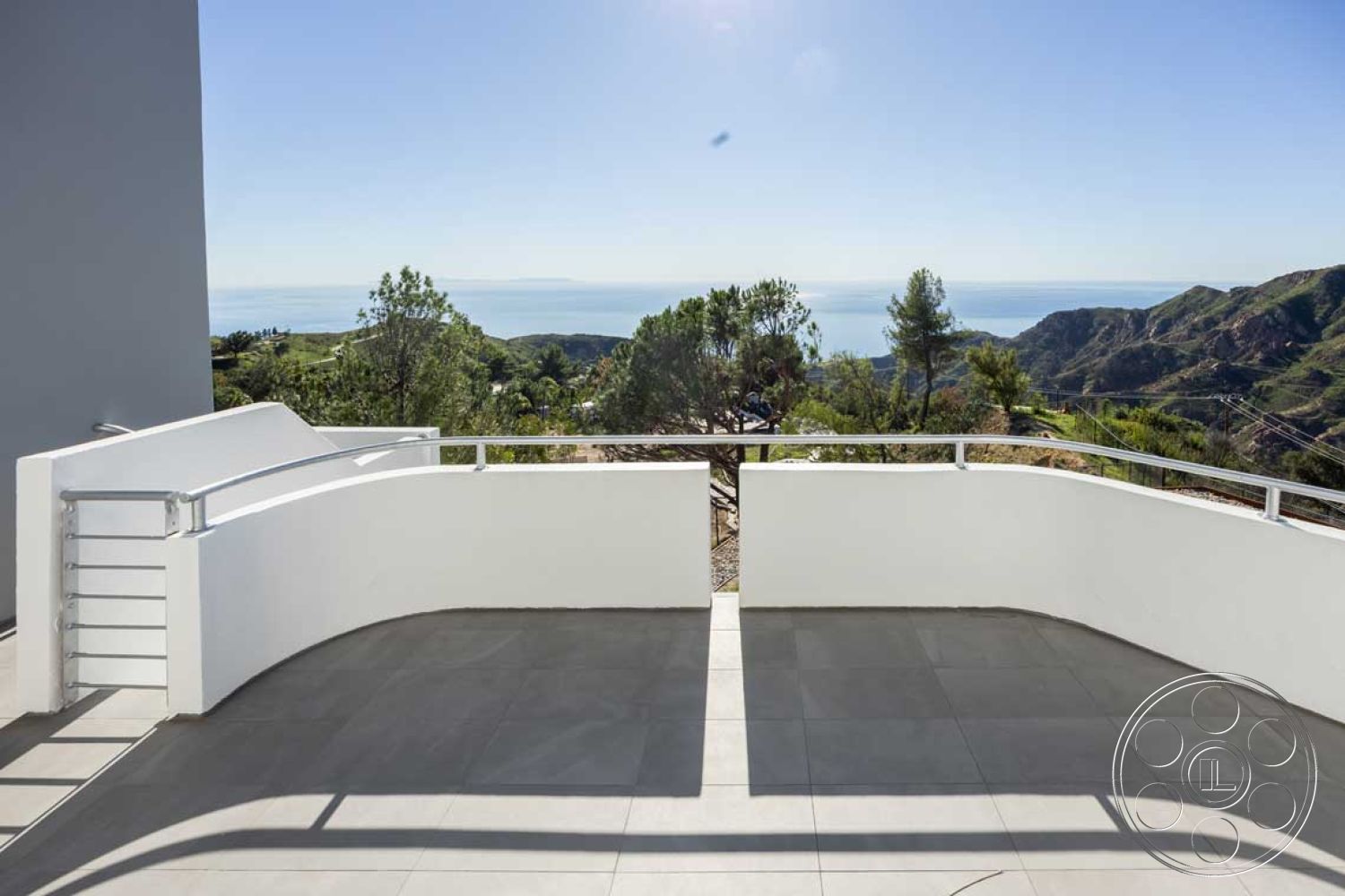 Modern 56 - glass railing, open-air patio, contemporary outdoor living space, natural light exposure, minimalist architectural style, exterior balcony, large format tile flooring, curved balcony design, landscaped hillside environment, smooth white stucco walls, concrete balcony floor, mountain and ocean view setting