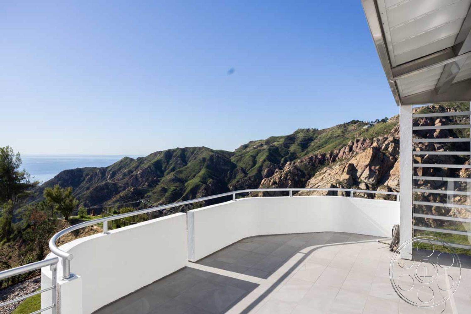 Modern 56 - minimalist design elements, modern architectural style, open outdoor space, sunlit terrace, natural light exposure, glass railing system, stucco wall finishes, exterior balcony with ocean view, rectangular balcony layout, slate tile balcony flooring, mountainous landscape setting, contemporary outdoor living area, smooth concrete wall support