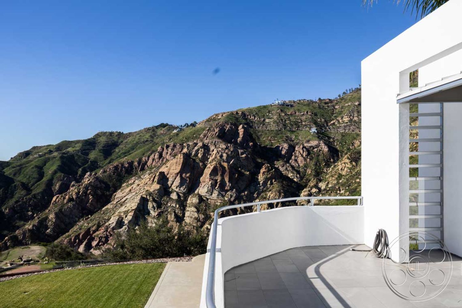 Modern 56 - exterior, white stucco walls, metal railing, sloping terrain, modern architectural style, mountain view setting, landscaped garden area, concrete patio flooring, curved patio design, floor-to-ceiling glass doors
