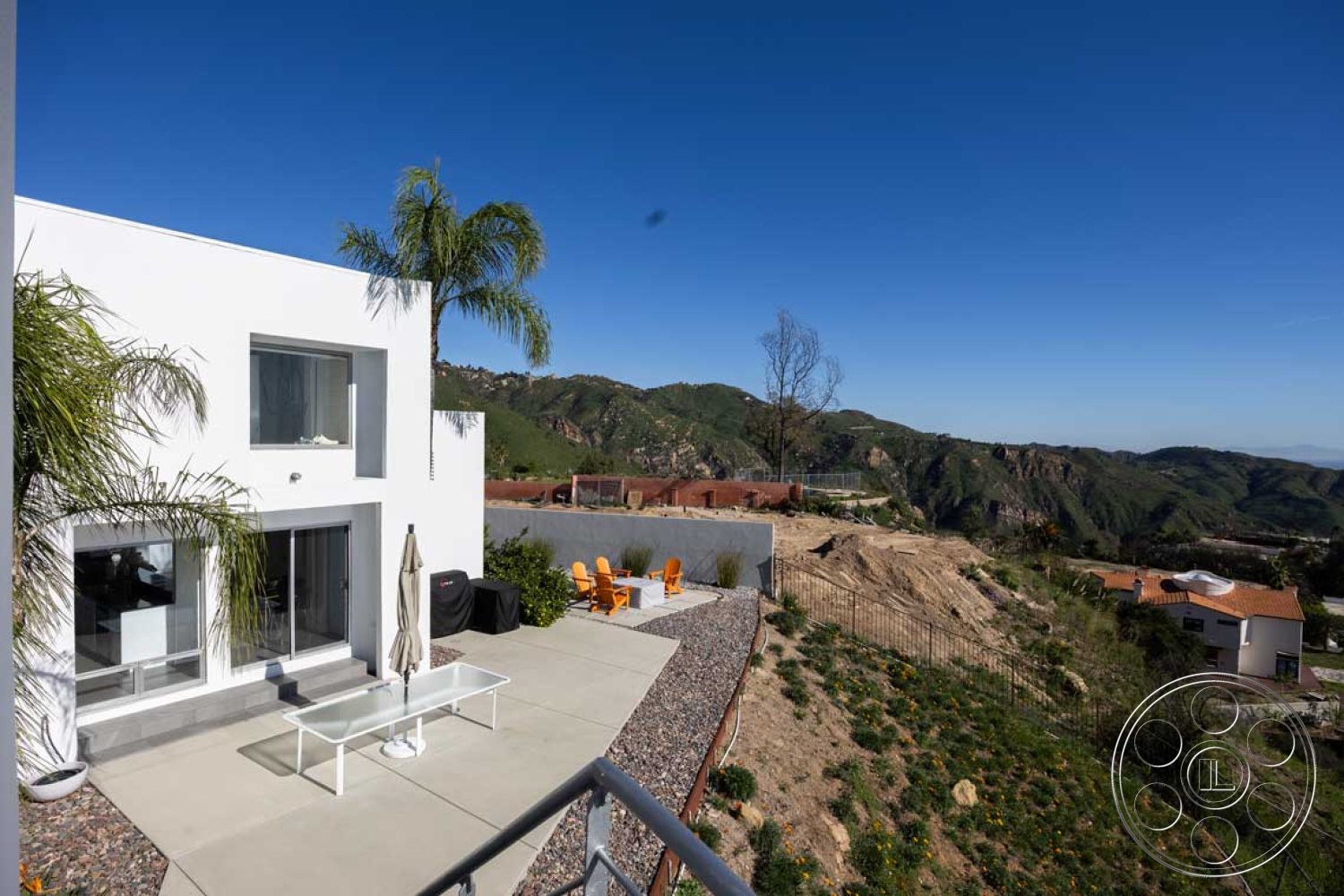 Modern 56 - glass sliding doors, minimalist exterior, concrete retaining wall, flat roof design, contemporary architectural style, urban hillside location, interior open floor plan, natural stone garden path, modern outdoor seating area, exposed aggregate concrete, concrete patio floor, tropical plant accents, outdoor leisure space, rectangular outdoor table, large panoramic windows, succulent garden landscaping, white stucco finish, panoramic mountain view, metal umbrella stand, residential exterior design