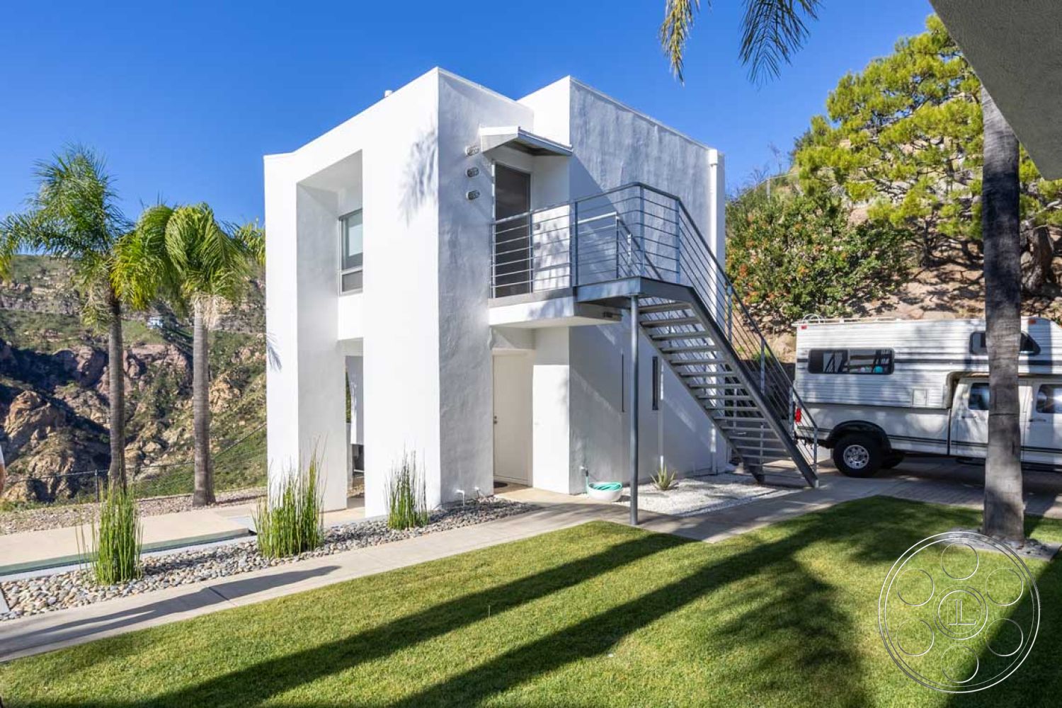 Modern 56 - outdoor living space, modern architectural style, tropical palm trees, clean lines and geometric forms, exterior white stucco walls, glass window panels, metal spiral staircase, hillside location with mountain view, landscaped garden with gravel, paved driveway with concrete pavers, low-maintenance grass lawn