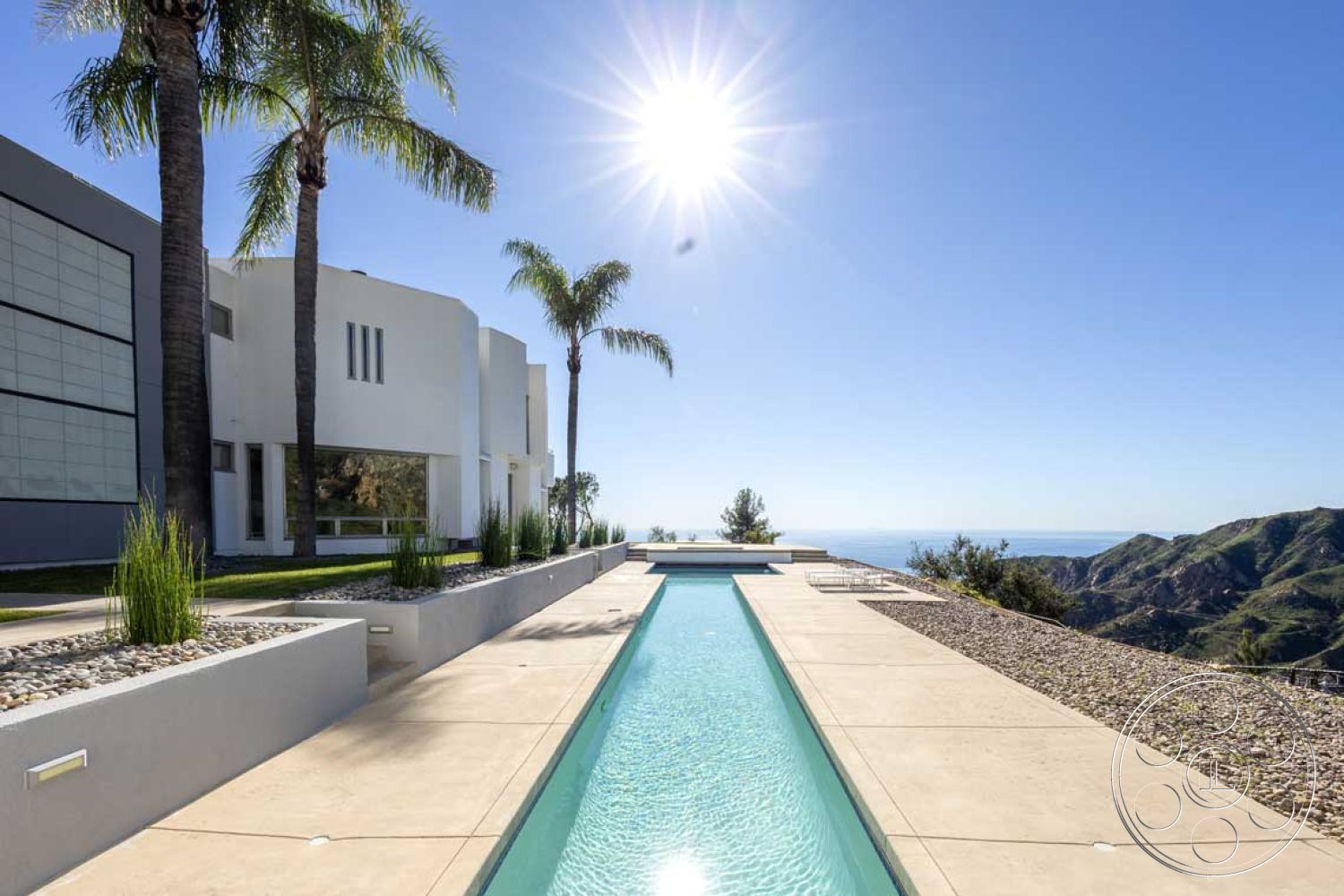 Modern 56 - rectangular swimming pool, gravel landscaping, large floor-to-ceiling windows, flat roof design, contemporary architectural style, exterior concrete patio floor, exterior concrete pool border, modern minimalist home, natural light-filled spaces, textured stone landscape border, luxury hillside location, palm trees in suburban setting