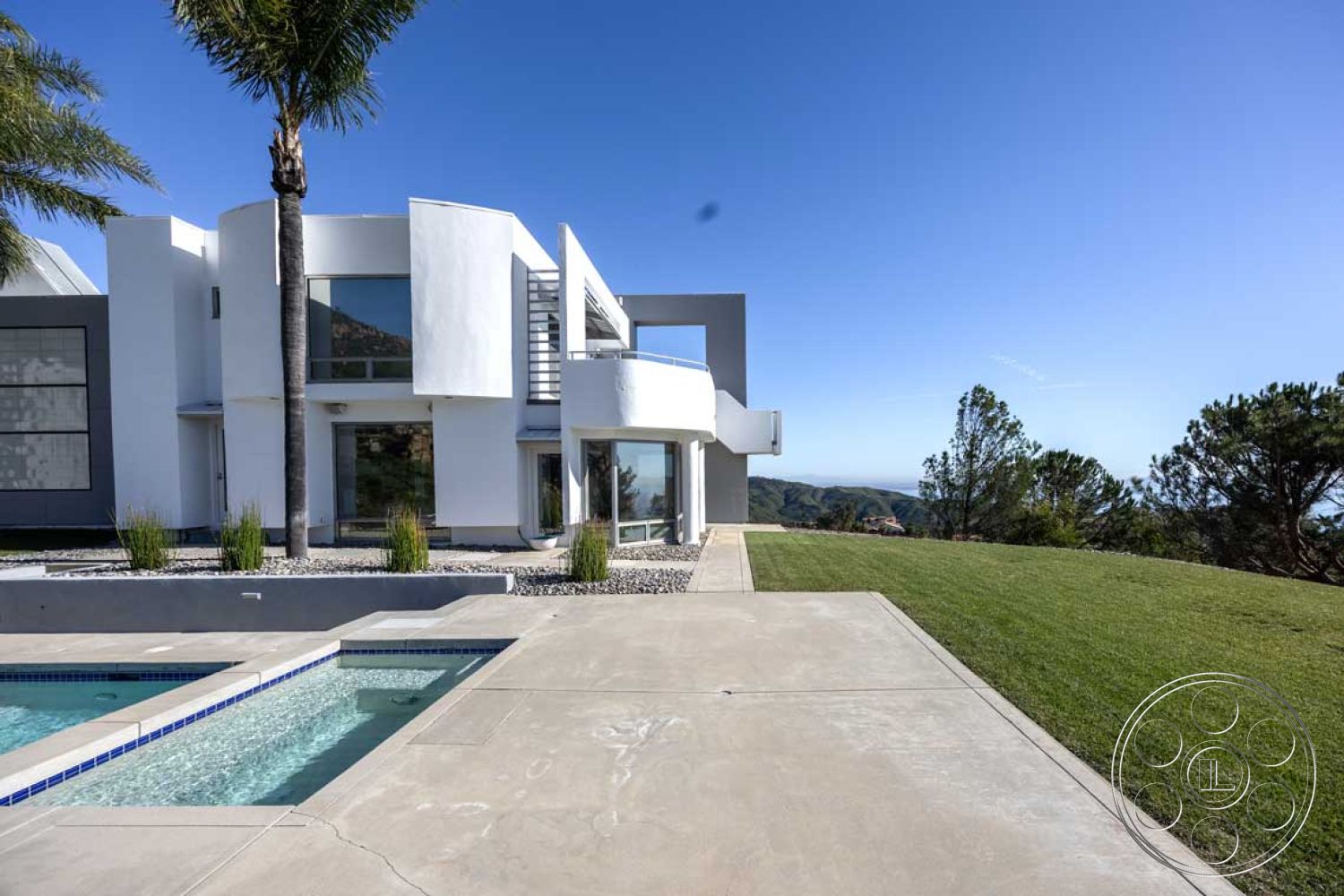 Modern 56 - floor-to-ceiling windows, modern architectural style, mountain view setting, exterior concrete patio floor, exterior white stucco walls, clear blue sky backdrop, rectangular pool with tile border, landscaped garden with grasses, gravel landscape decoration, palm trees in outdoor setting