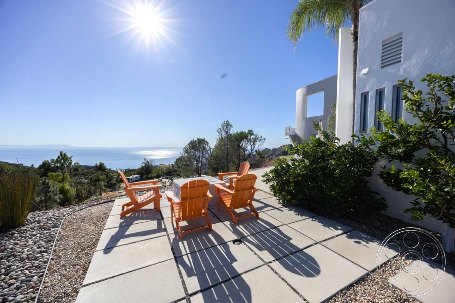 Modern 56 - modern outdoor furniture, landscaped hillside, concrete patio flooring, exterior white stucco walls, minimalist architectural style, contemporary outdoor area, rectangle patio shape, orange wooden Adirondack chairs, ocean view setting, planted garden area, clear sunny sky, boulder rock landscaping