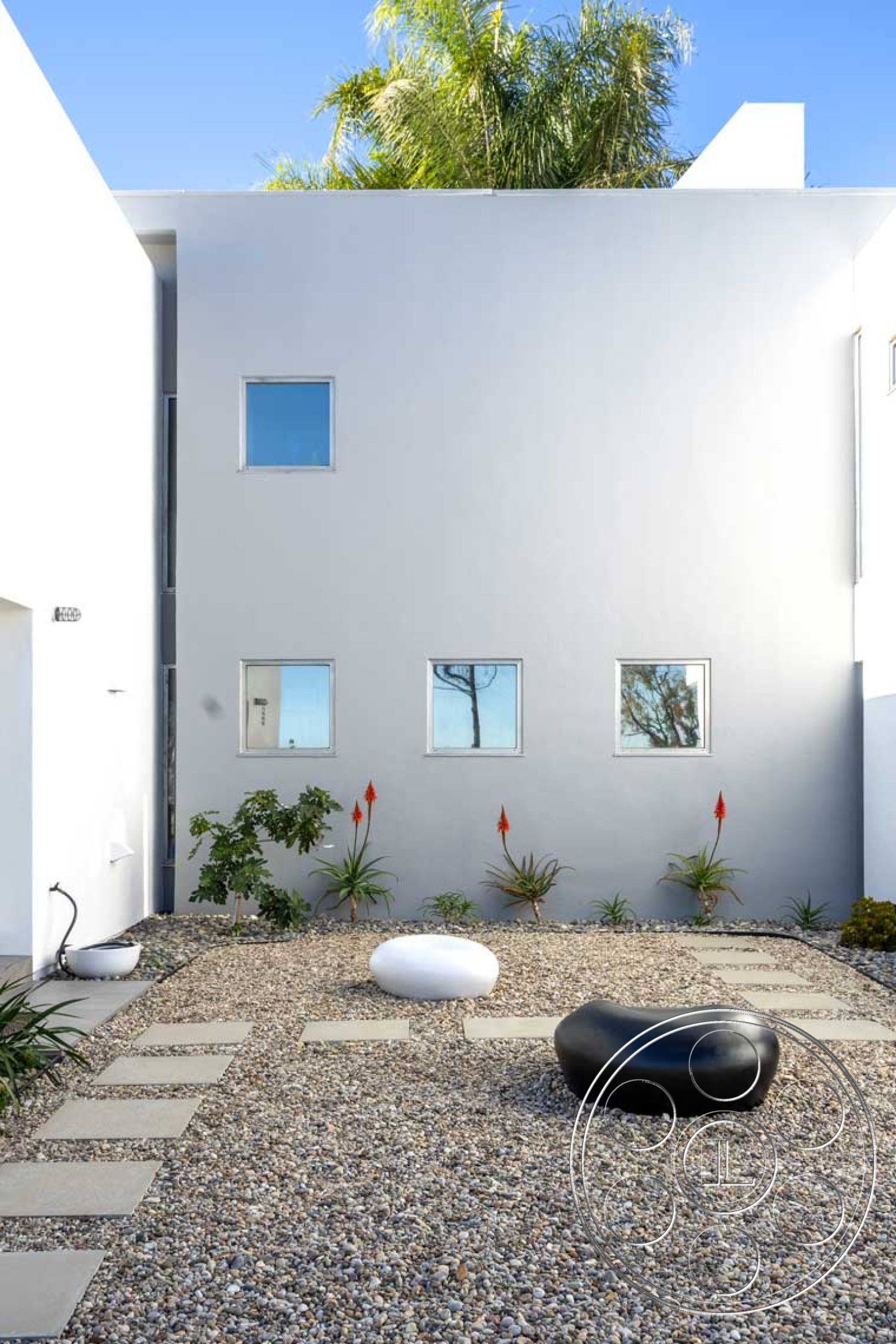 Modern 56 - exterior, white stucco walls, tropical landscaping, succulent plants, symmetrical layout, modern garden design, concrete stepping stones, gravel landscape, small square windows, minimalist outdoor seating, black sculptural stone seating, white sculptural stone seating