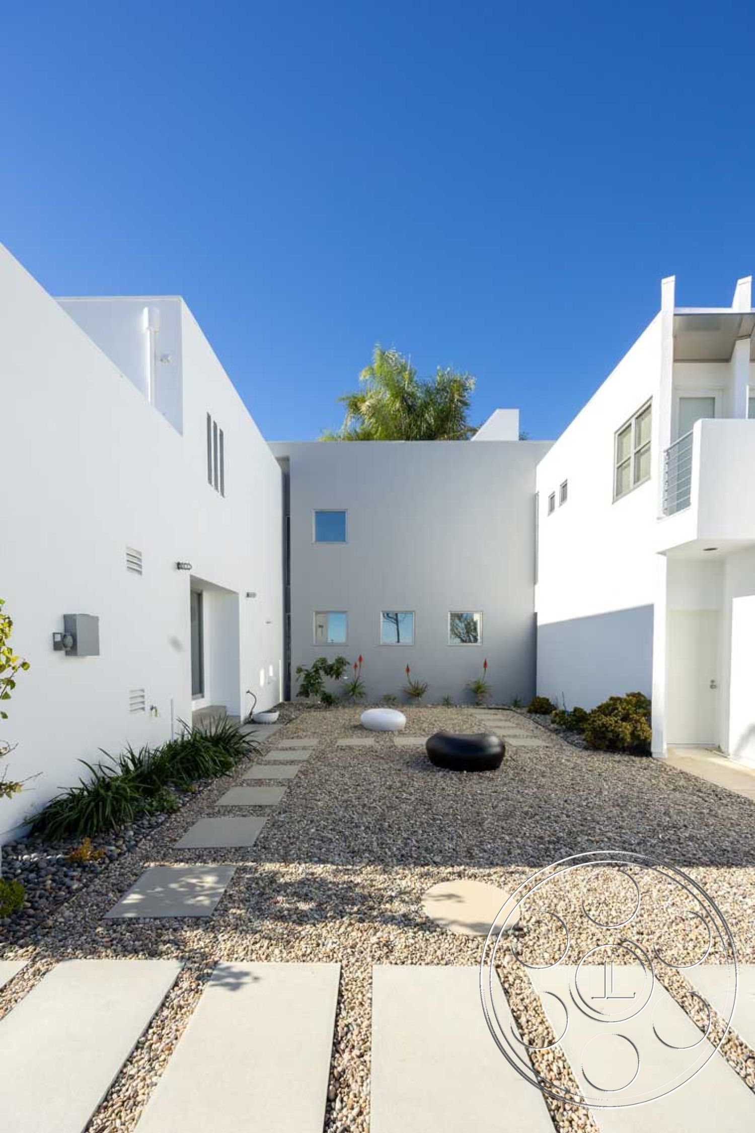 Modern 56 - hardscape elements, white stucco facade, concrete stepping stones, flat roof design, contemporary home design, urban courtyard setting, sunny outdoor environment, minimalist outdoor seating, gravel landscape flooring, horizontal window arrangement, geometric garden layout, modern exterior walls, small shrub landscaping, exterior wide window openings, light-colored stone aggregate, clean line architecture