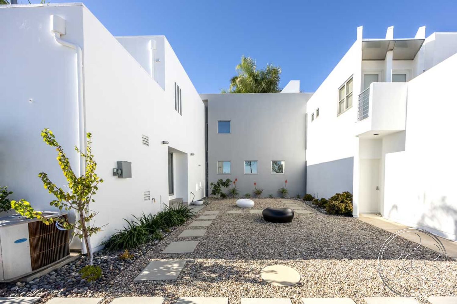 Modern 56 - exterior, white stucco walls, low-maintenance plants, air conditioning unit, small garden area, metal outdoor furniture, gravel landscaping, desert environment, flat roof design, minimalist architectural style, contemporary residential setting, rectangular outdoor space, horizontal sliding glass doors, concrete pathway stones, sparse modern landscaping, open courtyard layout, large square windows, modern building elements