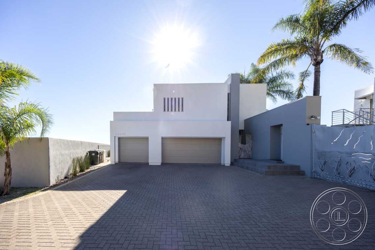 Modern 56 - paved driveway, white stucco walls, flat roof design, contemporary architectural style, landscaped garden beds, urban neighborhood setting, palm tree landscaping, modern home exterior, concrete steps leading to entrance, desert climate adaptation, horizontal window slits, large garage doors, grey feature wall, sunlight on exterior surfaces