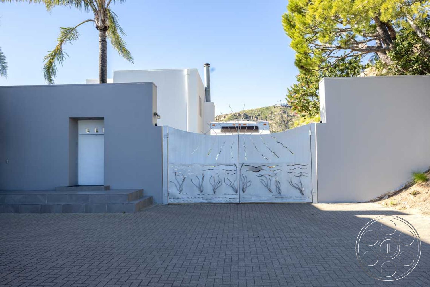 Modern 56 - exterior concrete driveway, exterior white stucco walls, exterior flat roof design, exterior concrete steps, exterior landscaping with palm trees, exterior hillside setting, exterior modern architecture, exterior steel gate with artistic design, exterior stone wall base, exterior clear sky backdrop