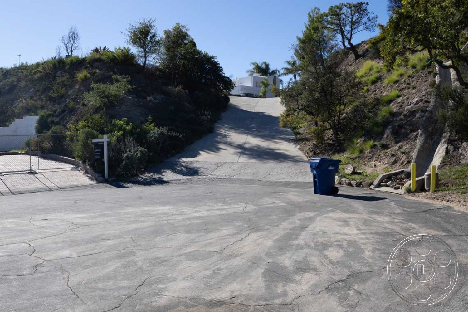 Modern 56 - retaining wall, surrounding trees, landscaped hillside, asphalt driveway, nature integration, residential exterior, urban hillside location, steeply sloped driveway, concrete driveway texture, mountainous terrain setting, fenced property access, blue trash bin