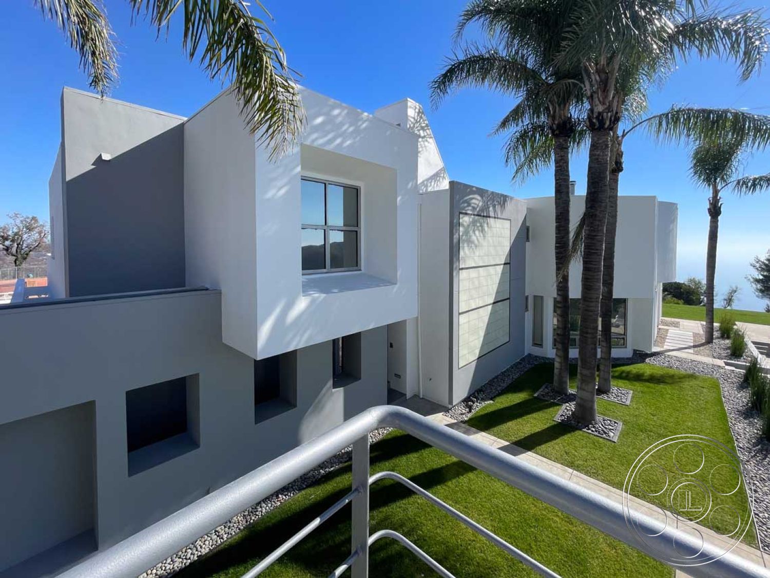 Modern 56 - exterior, minimalist design elements, city view, outdoor seating area, concrete pathway, modern architectural style, stucco façade, gray exterior walls, gravel ground cover, flat roof design, landscaped garden area, large rectangular windows, palm trees landscaping, geometric architectural shapes, smooth white plaster finish, hillside residence