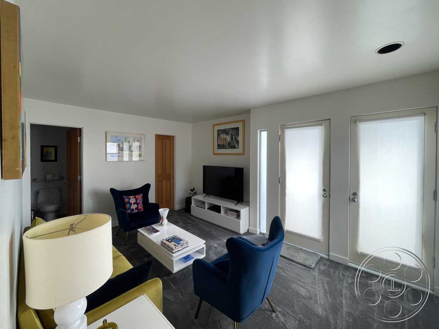 Modern 56 - neutral color palette, wooden door, modern coffee table, carpeted flooring, flat ceiling, simple wall art, accent pillows, interior living room, contemporary living space, exposed door frames, light-colored painted walls, dual sliding glass doors, blue armchairs