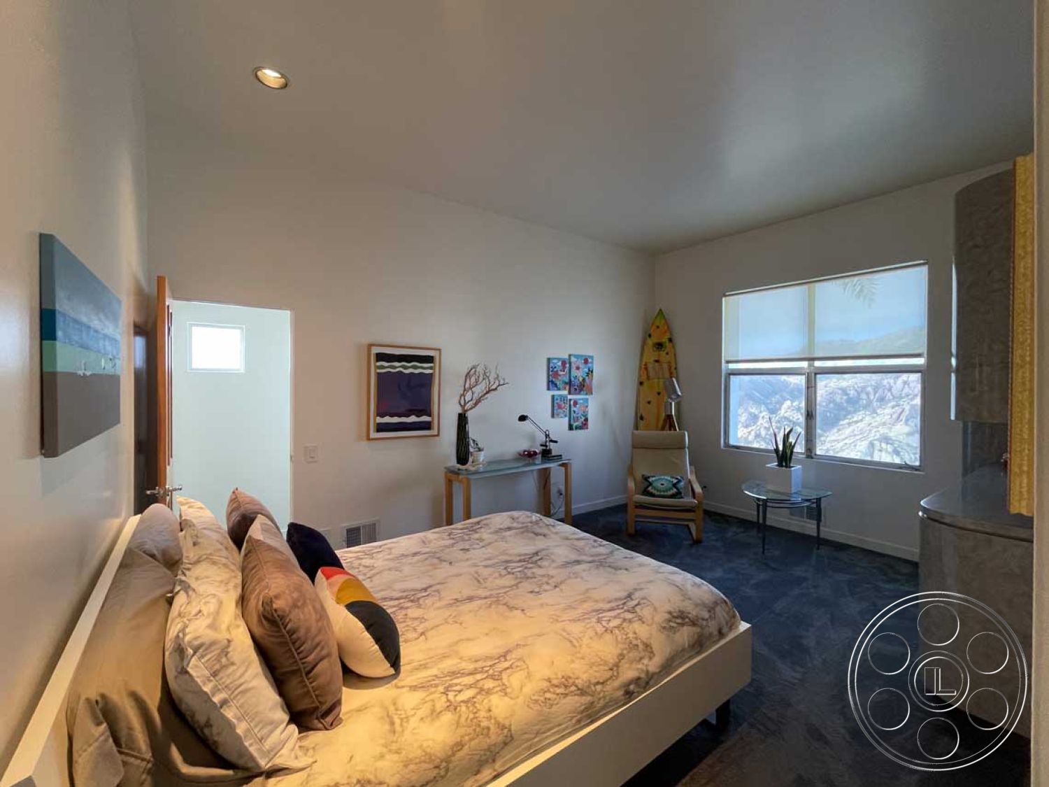 Modern 56 - floor-to-ceiling windows, mountain view, small potted plant, decorative throw pillows, marble bedside table, interior bedroom, painted drywall walls, modern desk lamp, carpet bedroom flooring, contemporary bed frame, painted canvas wall art, light wood accent chair, light-colored ceiling, colorful surfboard decor