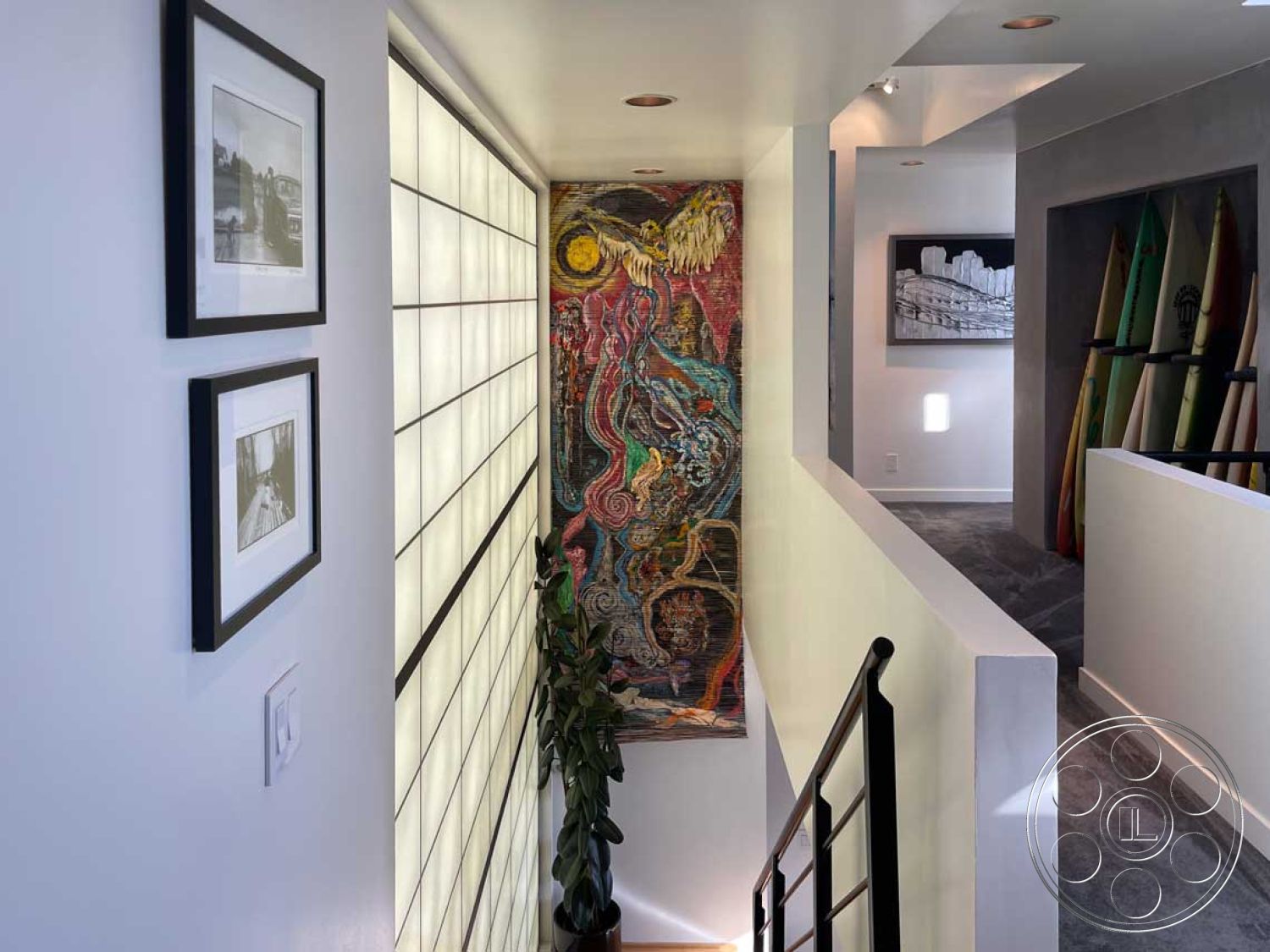 Modern 56 - dark metal stair railings, interior hallway with glass block partition wall, textured plaster walls with colorful artwork, soft carpet flooring in hallway, framed black and white photographs on walls, minimalist decor with open space design, modern lighting fixtures on ceiling, open landing area with artwork display, natural greenery with potted plant