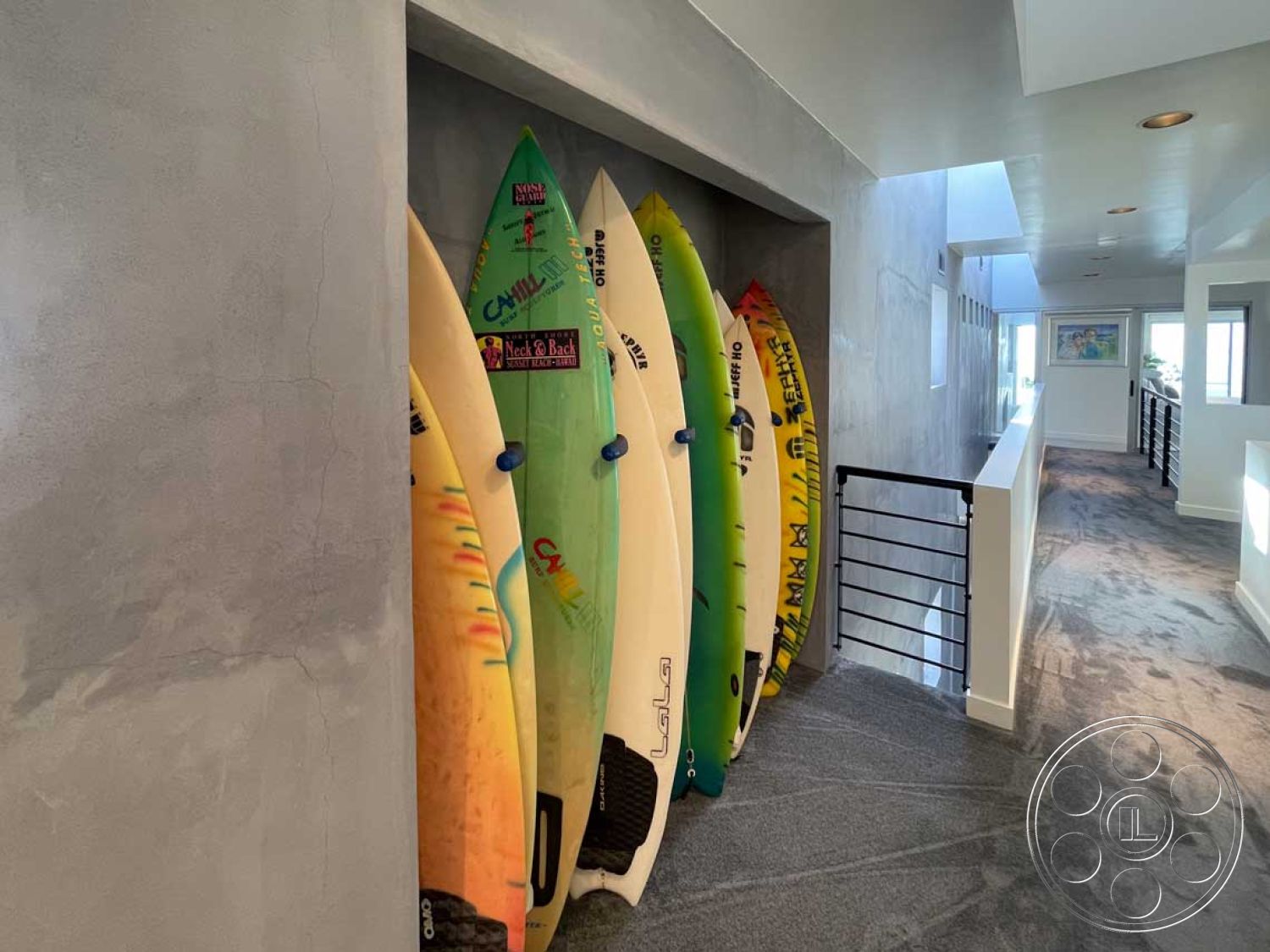 Modern 56 - high ceiling with recessed lighting, minimalist architectural style, open hallway layout, interior carpet flooring, exposed concrete wall finish, smooth plaster wall treatment, modern railing design, surfboard wall display, brightly colored surfboards, natural light elements