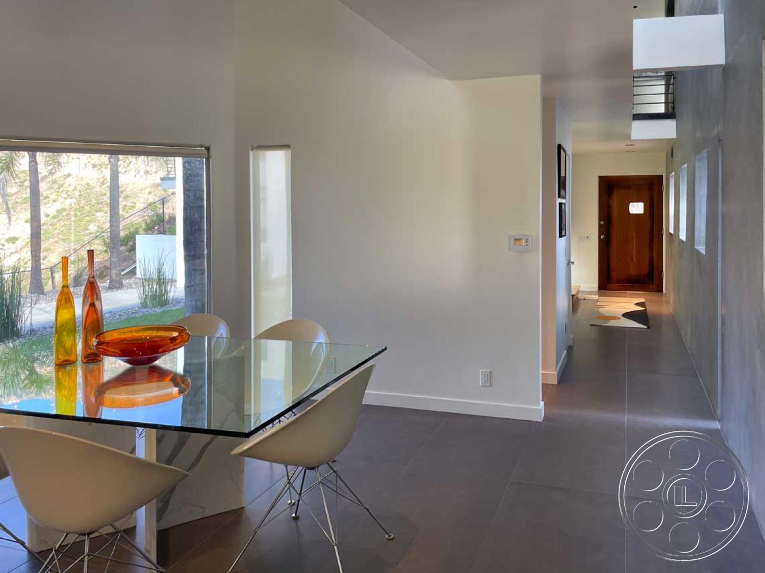 Modern 56 - neutral color palette, open floor plan, glass dining table, soft ambient lighting, large floor-to-ceiling windows, natural landscape view, minimalist architectural design, smooth white painted walls, ample natural light, contemporary dining room, Eiffel chair style chairs, earth-tone glass vase, oval decorative bowl, light gray porcelain tile floors, exposed concrete interior wall, modern wooden front door, sleek straight-edged forms