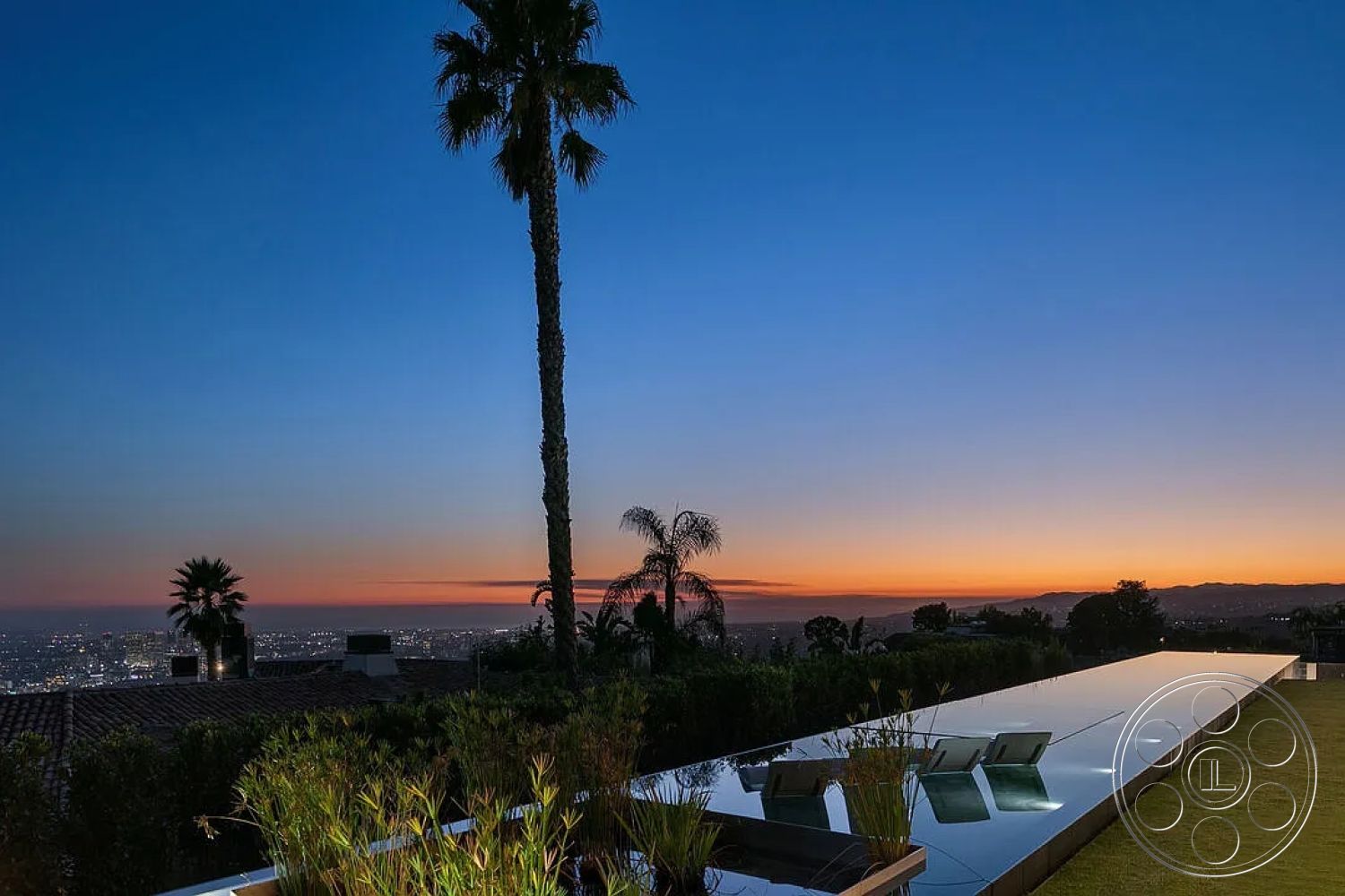 Modern 517 - exterior, concrete pool deck, modern lounge chairs, minimalist architectural style, luxurious outdoor living space, infinity pool with reflective surface, landscaped garden with tall grass, palm trees in soft evening light, hillside location with city skyline view, sunset lighting over the horizon, smooth concrete patio border, glass railing around pool area, urban rooftop with panoramic views, open sky at dusk