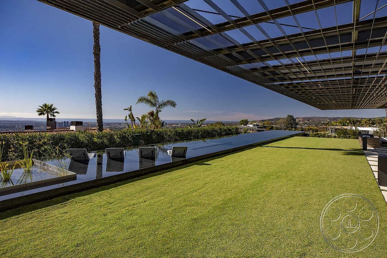 Modern 517 - exterior, sliding glass doors, outdoor lounge chairs, alfresco dining area, wooden deck flooring, glass partition walls, contemporary outdoor seating area, concrete pool border, panoramic city skyline view, luxurious contemporary style, integrated water features, landscaped green lawn, reflecting pool with minimalist design, overhanging metal roof structure, linear garden design with foliage, modern hardscape, palm trees in proximity, structural steel elements