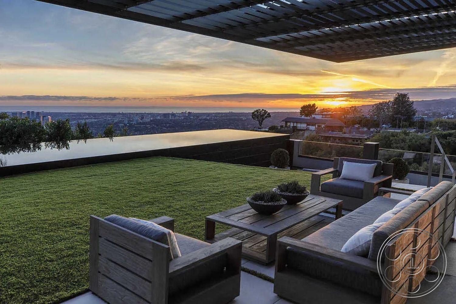 Modern 517 - exterior, sunset backdrop, city skyline view, artificial turf lawn, wooden outdoor furniture, concrete patio flooring, minimalist patio design, metal pergola structure, stainless steel outdoor railing, open air living space, glass infinity pool edge, contemporary landscape design, natural stone accent details