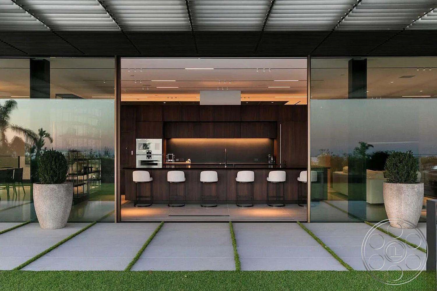 Modern 517 - interior kitchen with dark wood cabinetry, interior open space layout, modern minimalist architectural style, interior recessed lighting in ceiling, exterior glass wall opening to outdoor patio, interior bar seating with white upholstered stools, exterior stone pavers for patio flooring, exterior landscaped grass area, exterior contemporary outdoor living area, glass planter with greenery, square-shaped concrete slabs, interior warm kitchen lighting, exterior views of surrounding landscape, interior high ceiling with structural beams, exterior patio space for entertaining, concrete walkway with grass inlays