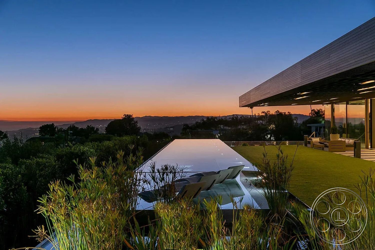 Modern 517 - exterior, glass sliding doors, natural surroundings, modern landscaping, stone patio, green lawn, sunset view, outdoor lounge area, open-air design, city skyline view, landscape lighting, contemporary home, infinity pool, large floor-to-ceiling windows, reflective water surface, elevated location, minimalist architecture, roof overhang, wood plank ceiling, built-in outdoor seating