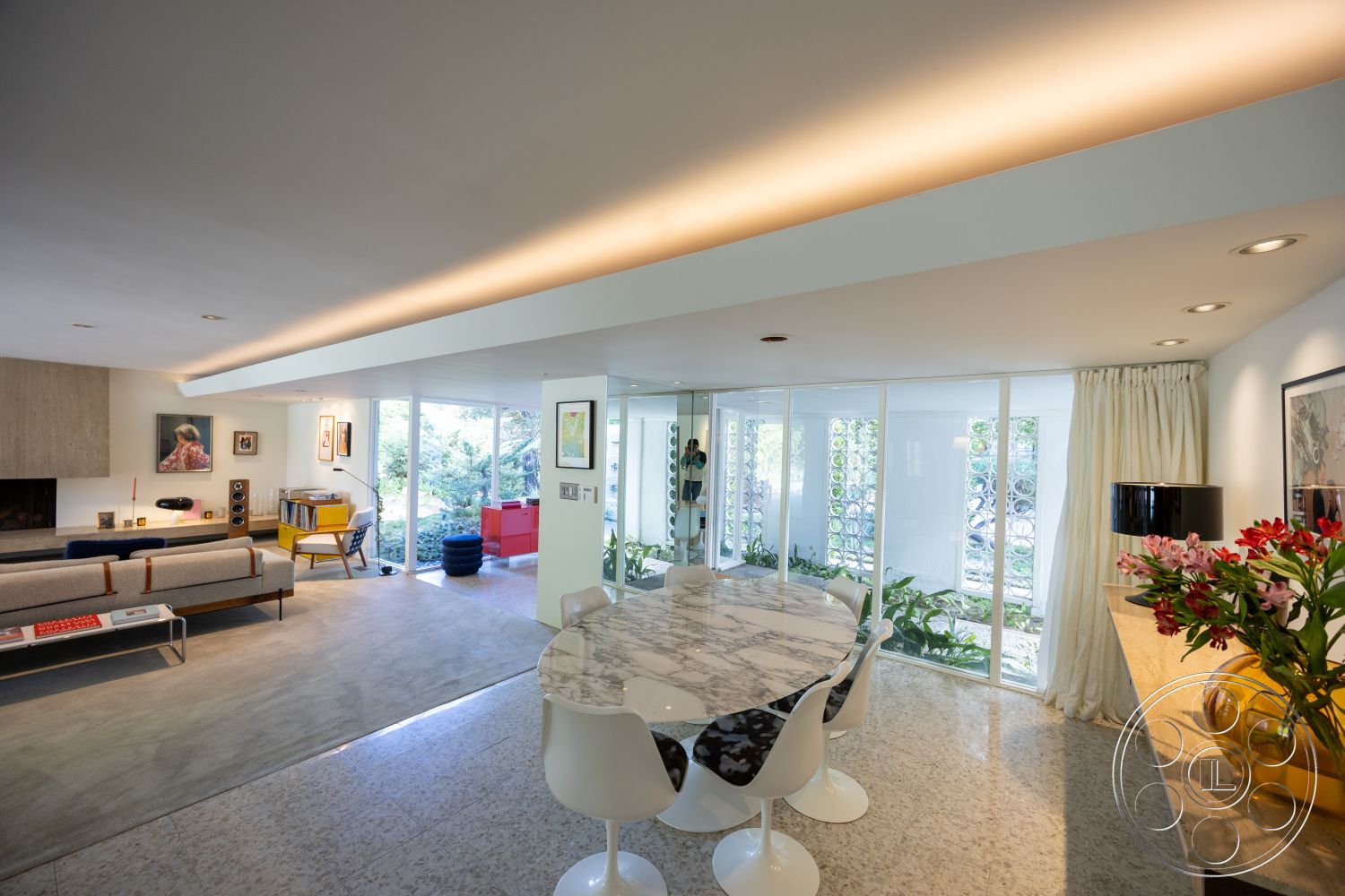 MCM 27 - interior pendant lighting fixtures, interior open floor plan, interior recessed lighting fixtures, interior floor-to-ceiling glass windows, interior marble dining table, interior polished terrazzo flooring, interior concrete fireplace surround, interior modern art on walls, interior minimalistic furniture design, interior upholstered mid-century modern sofa, interior bright green plant decor, interior light wood accent shelves, interior soft white curtains, interior black and white patterned dining chairs, interior exposed concrete wall, interior curved dining table