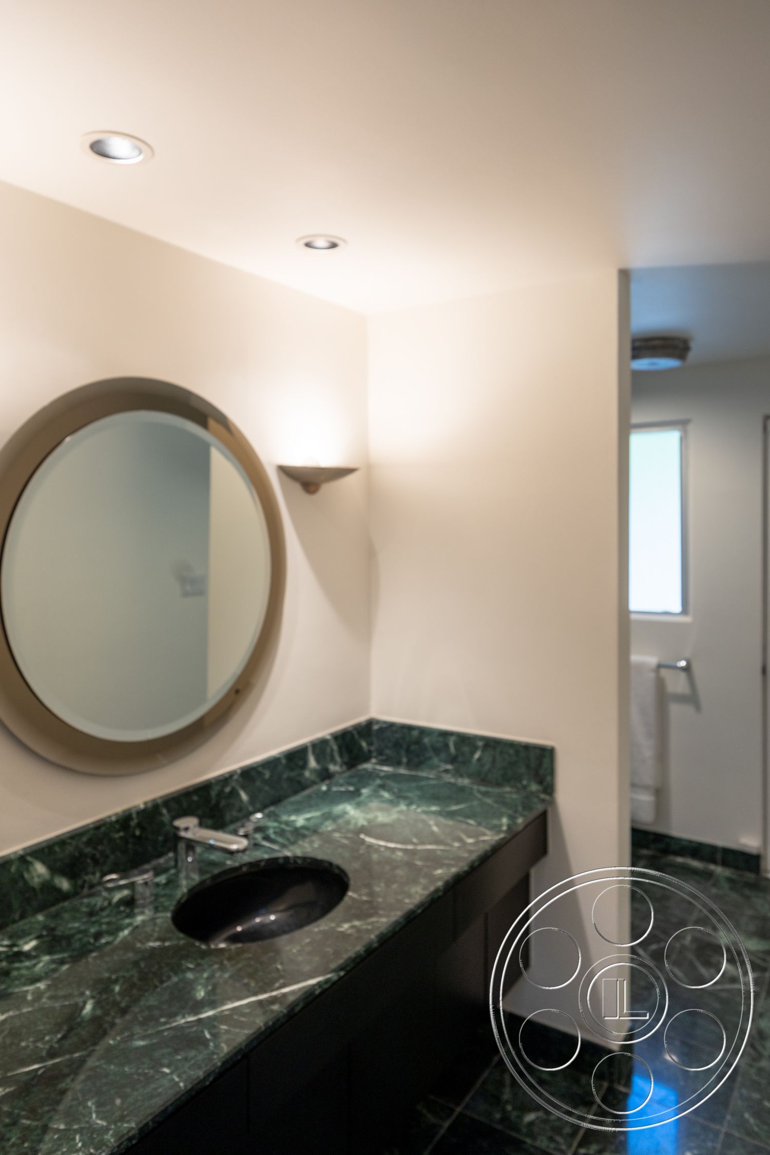 MCM 27 - minimalist design, dark cabinetry, polished marble flooring, natural light from window, recessed ceiling lighting, interior bathroom, white painted walls, green marble vanity countertop, black sink basin, modern circular mirror