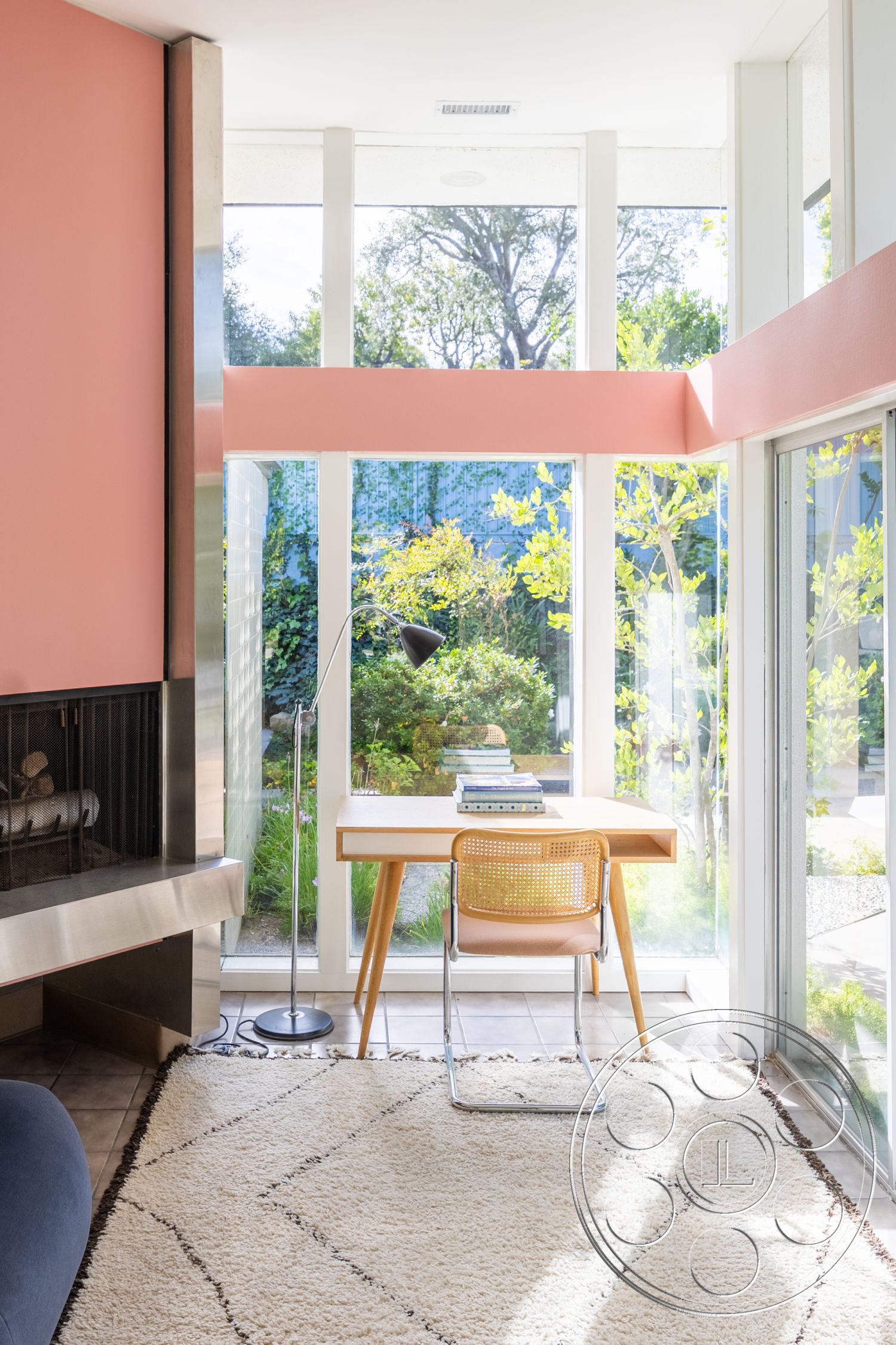 MCM 27 - minimalist design, textured area rug, bright natural light, functional workspace, contemporary architecture, casual seating area, indoor greenery, ceramic floor tiles, open-plan layout, woven rattan chair, interior glass walls, exterior garden view, pink painted accent wall, metal fireplace surround, hardwood desk with natural finish