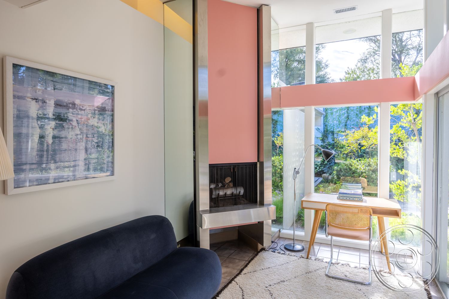 MCM 27 - hardwood flooring, open floor plan, framed artwork, functional workspace, green garden view, light color palette, pink accent wall, modern minimalist design, wood beam ceiling, contemporary lounge seating, natural light abundance, glass window walls, integrated lighting features, concrete fireplace surround, stylish desk area