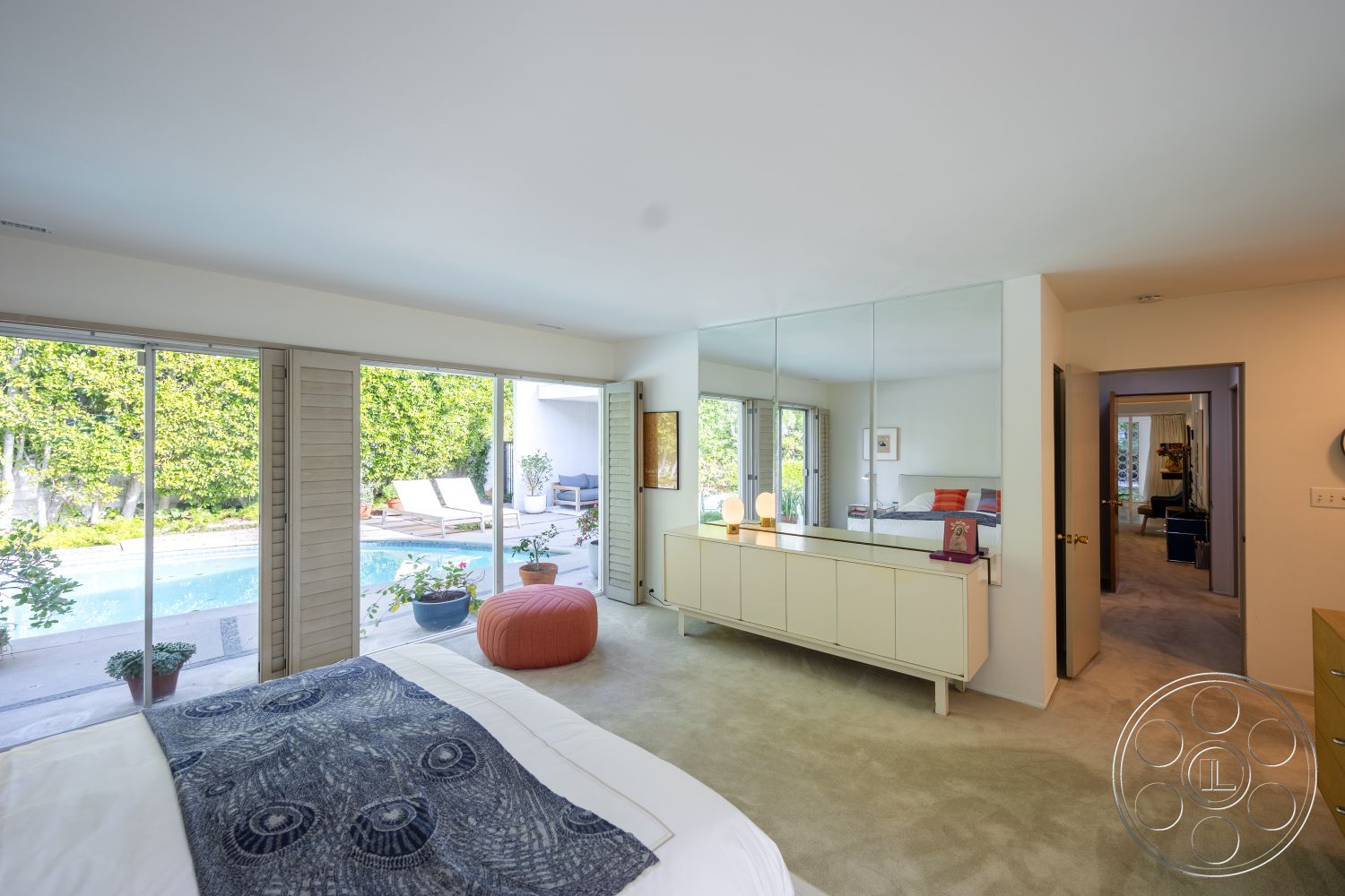 MCM 27 - open floor plan, minimalist design elements, floor-to-ceiling windows, textured wall treatment, suburban backyard, soft color palette, contemporary lighting fixtures, rectangular pool shape, plant-filled garden view, glass partition walls, exterior pool area, carpet bedroom flooring, sliding glass patio doors, indoor-outdoor living space, modern dresser with mirrored surface, vaulted ceiling in bedroom, exposed electrical outlets, simple curtain window treatments, lounge seating by the pool, neutral-toned carpeting