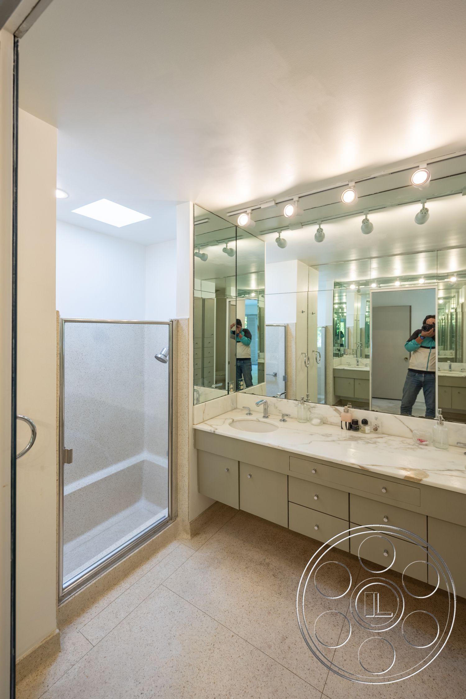 MCM 27 - neutral wall colors, marble countertop, large wall mirrors, modern bathroom lighting, glass shower doors, minimalist bathroom design, interior bathroom, white painted walls, skylight ceiling, tile bathroom flooring, contemporary faucet fixtures, built-in bathroom storage, spacious bathroom layout, exposed shower walls, mirrored vanity cabinets, polished stone shower bench, rectangular walk-in shower, clean lines in cabinetry