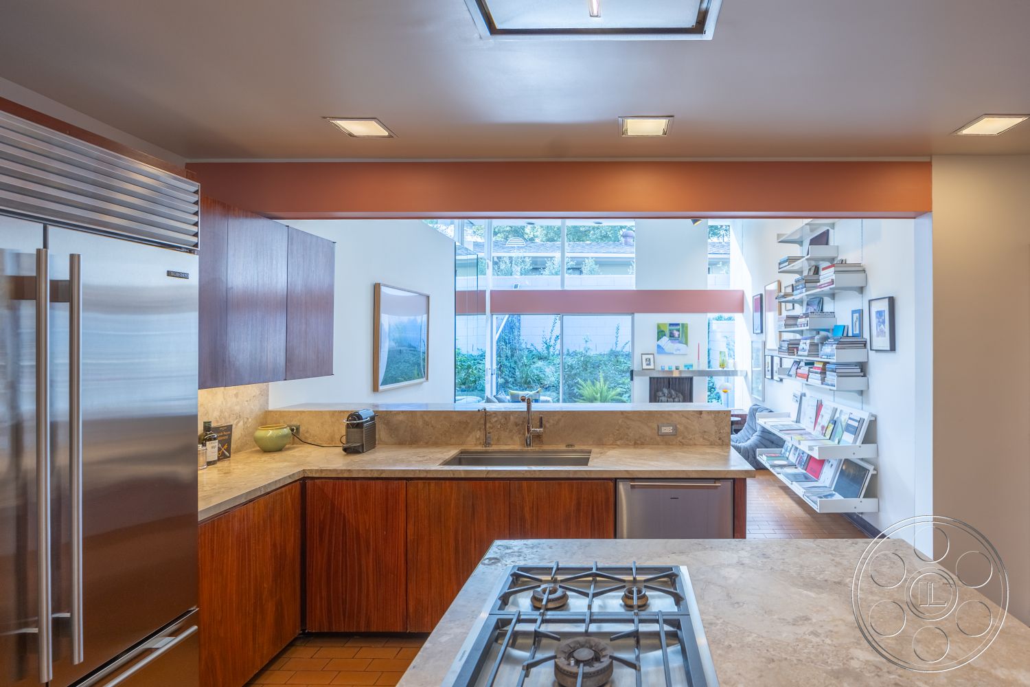 MCM 27 - gas cooktop, open concept design, minimalistic decor, textured plaster ceiling, stainless steel refrigerator, ceramic tile floor, marble kitchen countertops, large windows providing natural light, interior kitchen with wooden cabinetry, modern kitchen sink, contemporary kitchen layout, built-in bookshelf on wall, garden view from kitchen, natural wood tones in cabinetry, indoor plant visibility from windows, efficient kitchen workspace