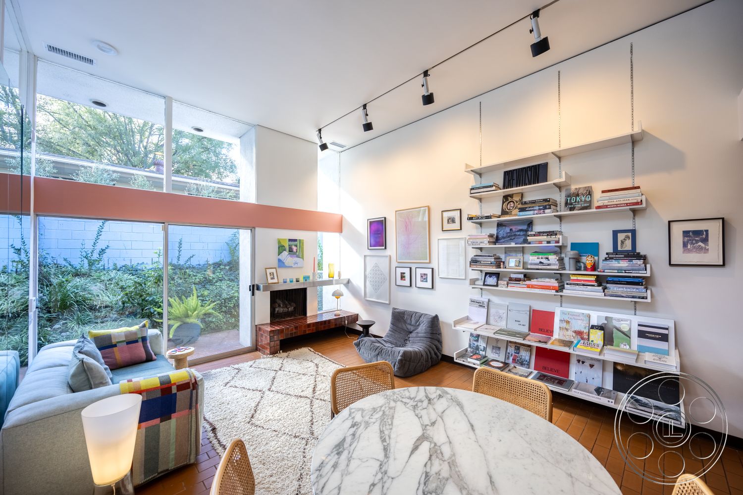 MCM 27 - minimalist decor, neutral color palette, natural light, textured area rug, interior space, round marble dining table, exposed ceiling beams, plush seating area, recessed lighting fixtures, brick fireplace surround, soft carpet flooring, modern wall art, glass wall with garden view, floating shelf for books, contemporary accent chair, colorful plaid throw pillows, open living area, compact living room layout