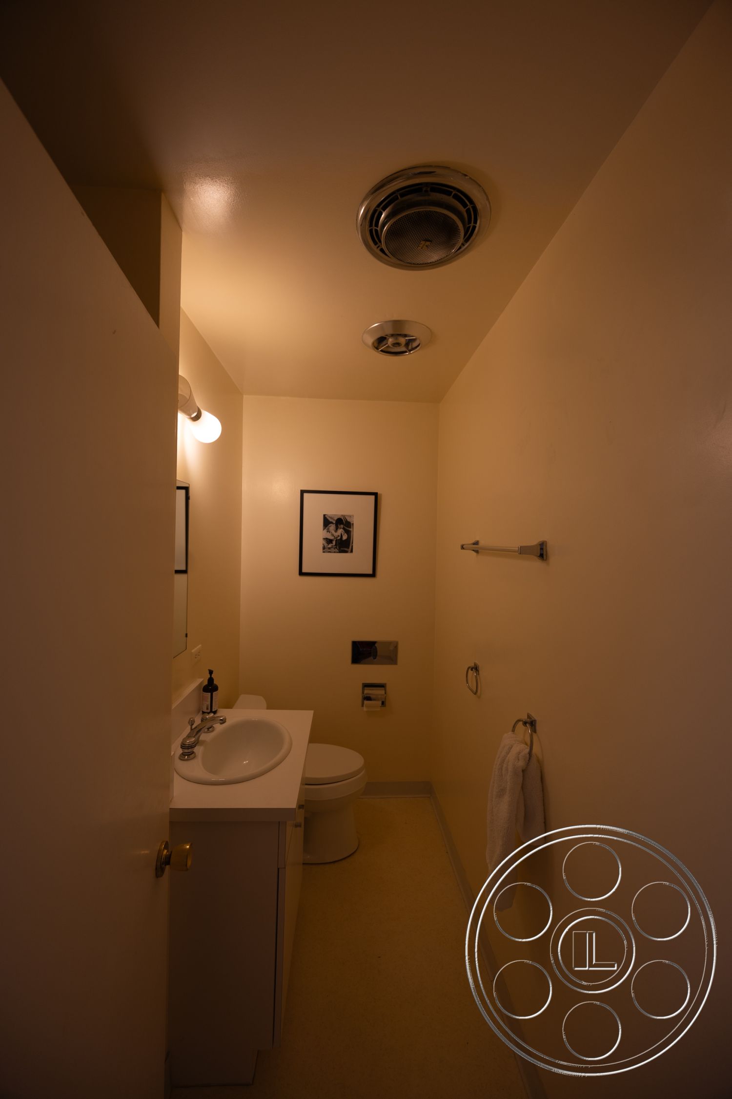 MCM 27 - minimalist design, sconce lighting, framed wall art, vinyl flooring, neutral color scheme, accessible layout, ambient lighting fixtures, interior bathroom, white painted walls, mirror above sink, compact sink vanity, toilet with flush tank, mounted towel bar, standard ceiling height, modern bathroom accessories