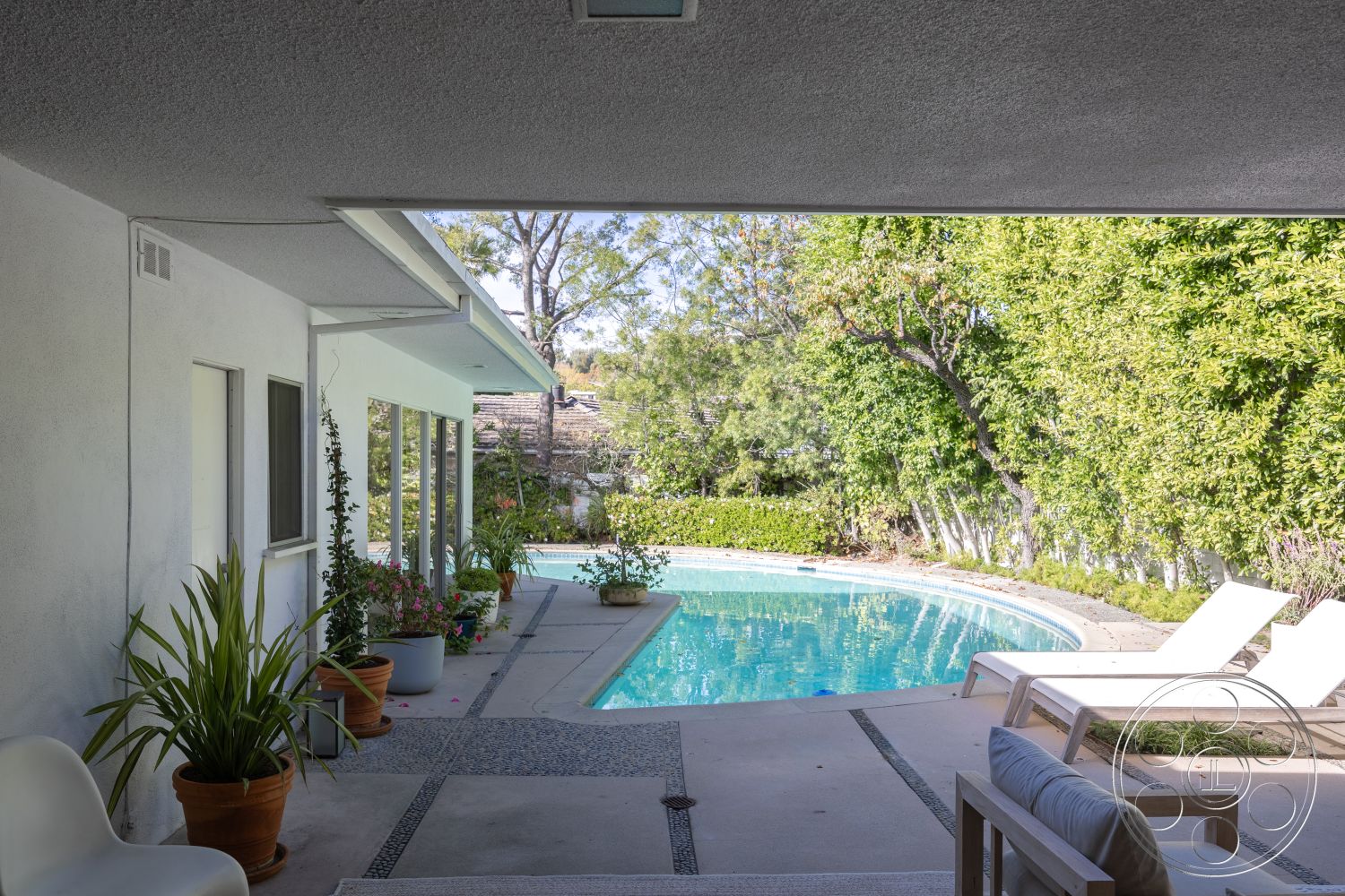 MCM 27 - exterior, potted plants, glass sliding doors, outdoor seating area, sun loungers, natural sunlight, concrete pool deck, canopy of trees, oval swimming pool, modern home design, stucco wall finish, urban backyard setting, tile patio flooring, landscape with hedges, elevated positioning