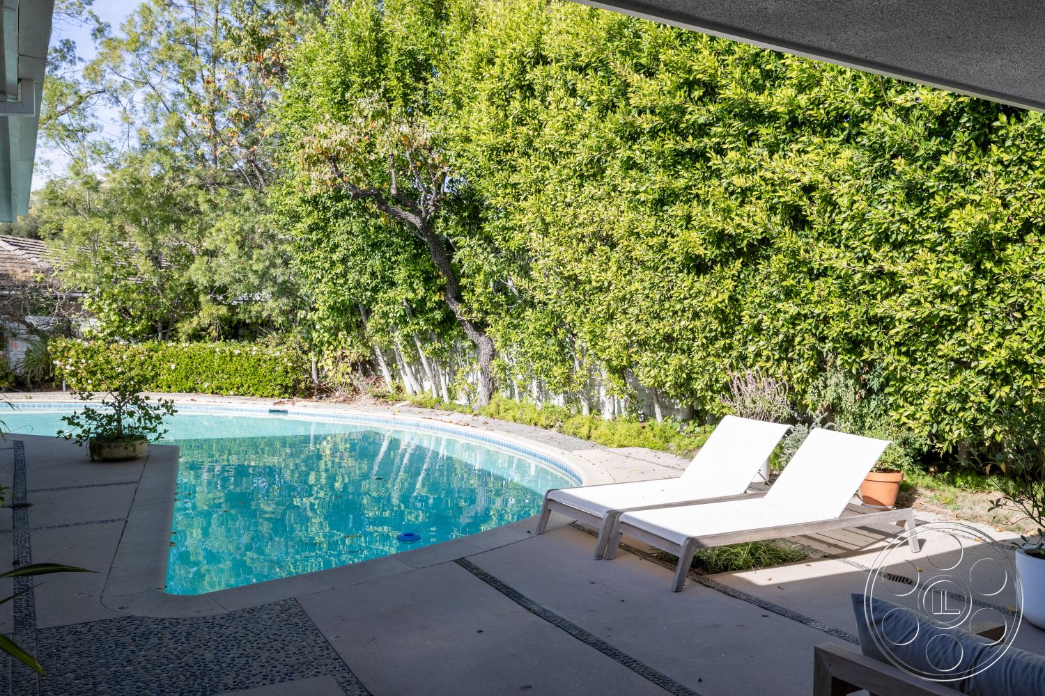 MCM 27 - white lounge chairs, sunny outdoor space, oval swimming pool, exterior concrete pool deck, tranquil pool area, landscape greenery setting, textured pebble concrete border, surrounding hedge landscaping, neutral patio flooring, modern poolside design
